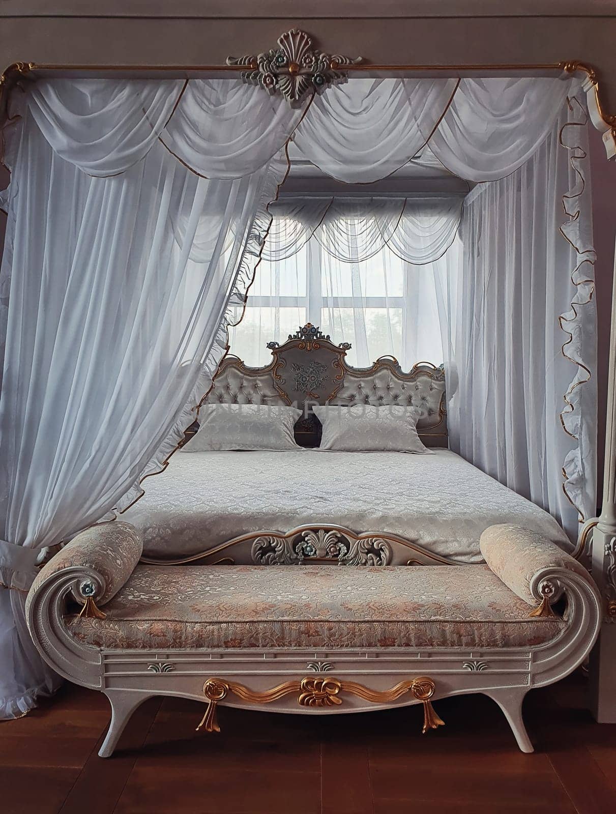 Ancient bedroom furniture style, medieval king bed, near the window, white curtains canopy and gold details. Close up background of a beautiful room luxuriously decorated for prince or princess.