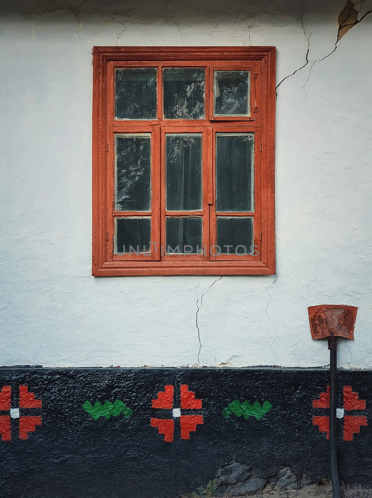 Brown colored wooden window framed into a cracked wall painted with light blue lime. Closeup architectural details of an old, traditional house in Moldova culture. Rural building facade, vintage home.