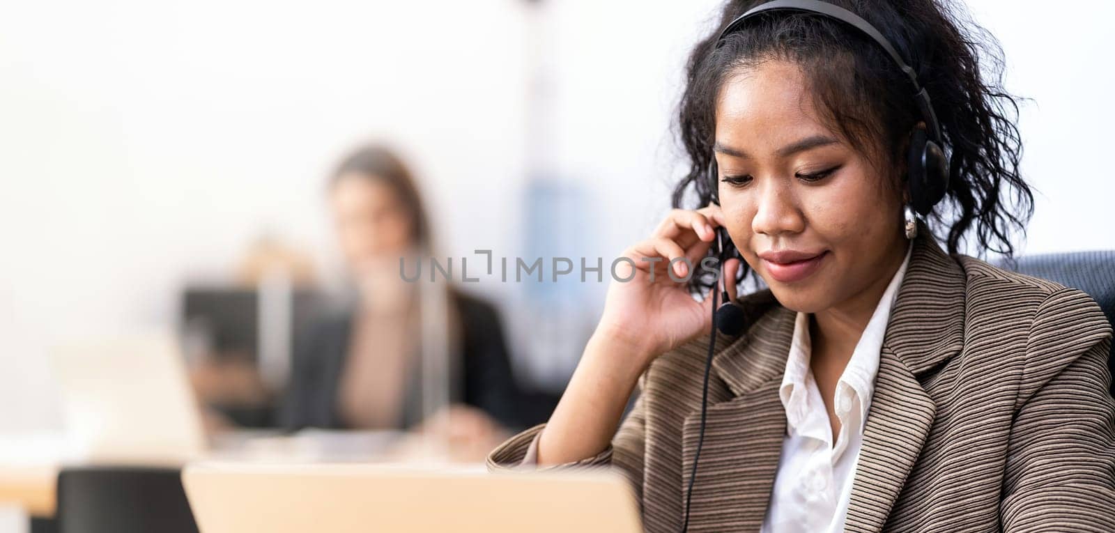 Panorama Young adult friendly confidence operator Mixed race of African asian woman with headsets working in a call center with her colleague in background. Call center and telemarketing sale concept.