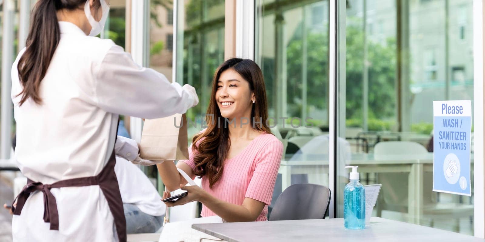 Panoramic view of attractive woman female customer take take out food bag order from waitress wear face mask. Take away or take-out food service concept in new normal after coronavirus pandemic.