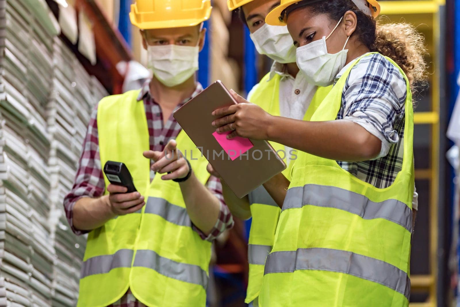 Interracial team Asian African Caucasian working on inventory use barcode scanner and digital tablet in distribution center. They wear face mask prevent from COVID-19. Warehouse and hygiene concept.