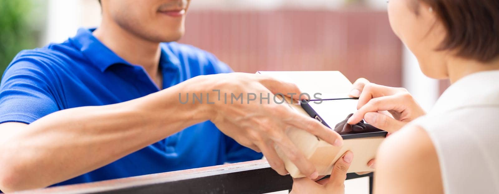 Panoramic Asian woman sign electronic signature to portable mobile device after receive packge from male delivery man in blue shirt. Package shopping delivery and digital sign concept.