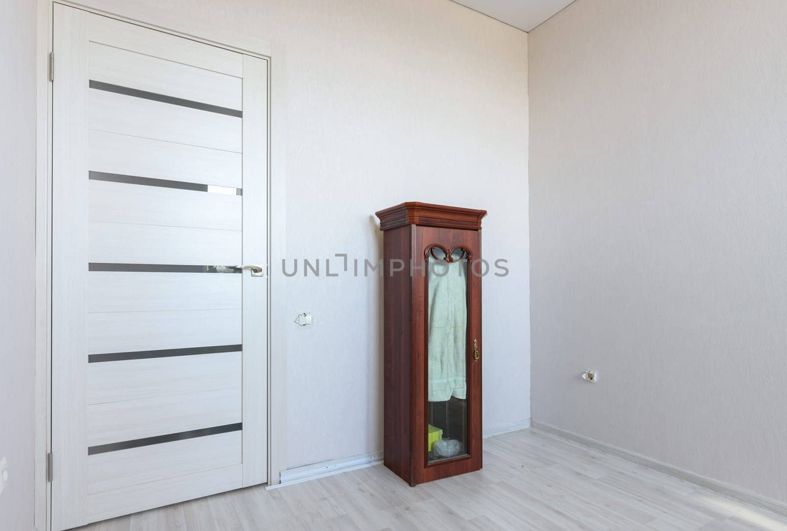 A fragment of a small bedroom in an apartment with poor furniture, a view of the front door and a locker