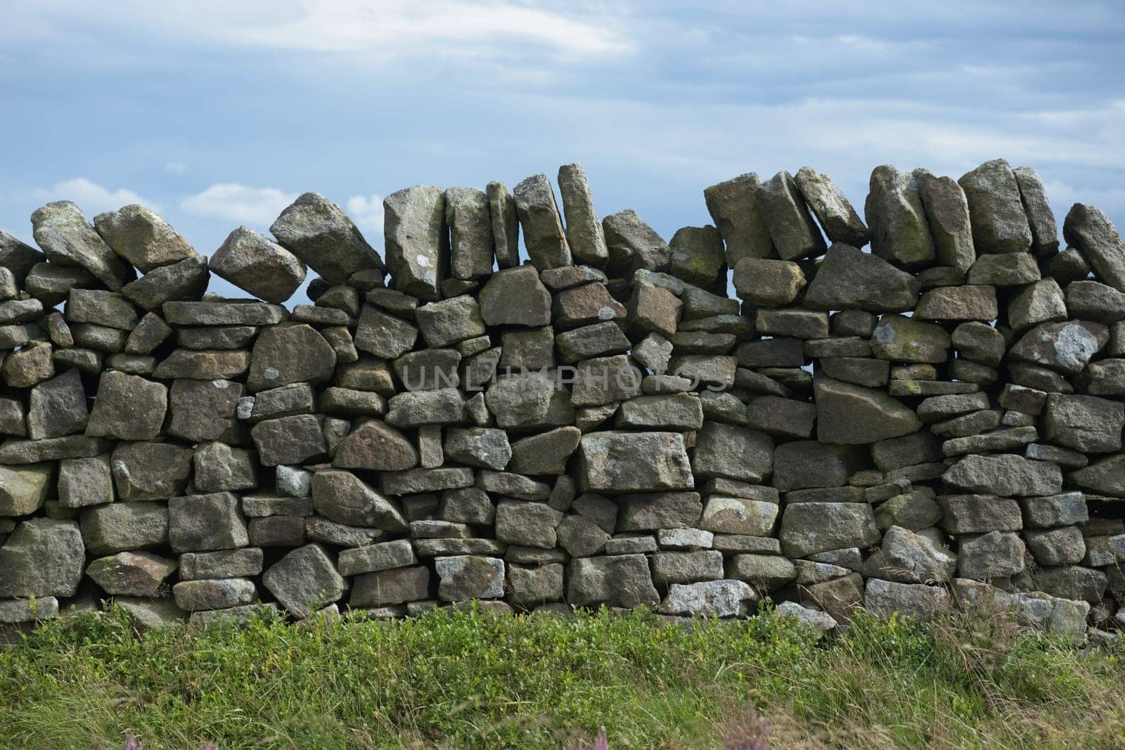 3 - Plain abstract background texture of dry stone wall. Close up of random mix of stone brickwork. Cloudy background and plants in foreground.