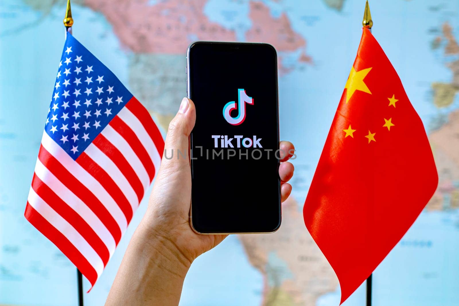 Calgary, Alberta, Canada. Sep 8, 2020. A person holding an iPhone with the TikTok app screen next to a USA and China flags on a world map.
