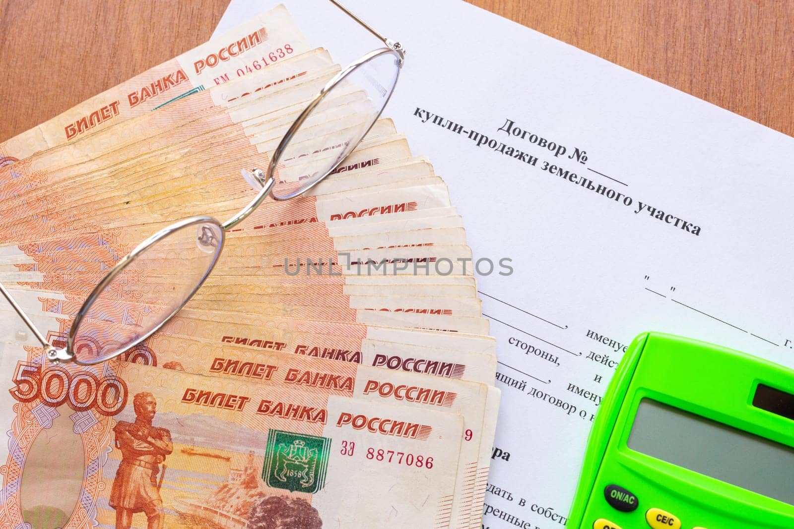 On the table there is a contract for the sale of a land plot, a bundle of money, a calculator and glasses