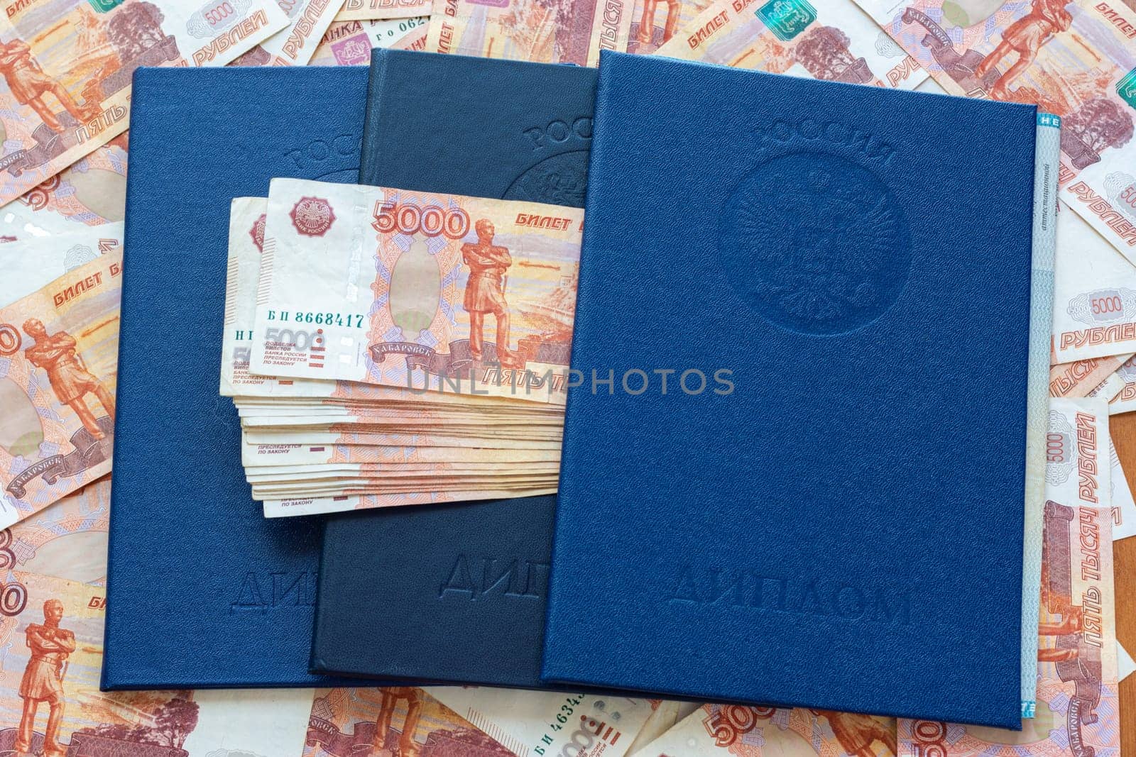 Three blue higher education diplomas lie in the background from the money, a bundle of money sticks out between the diplomas