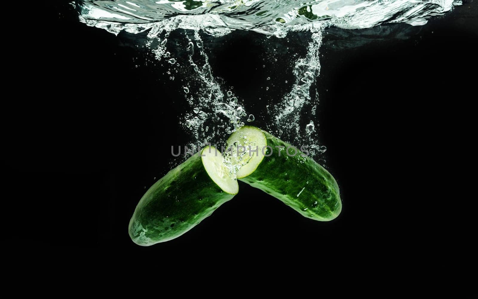 Cucumber cut in half splashing water isolated onblack background. Healthy food concept