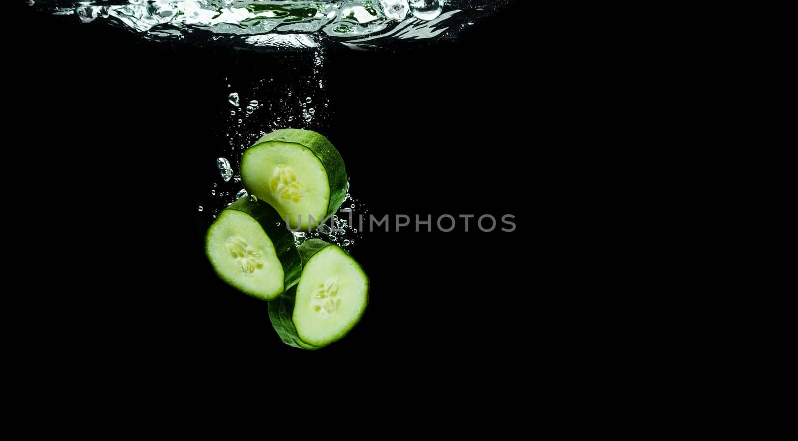Sliced bio cucumber splashing water isolated on black background. Skin moisturizing cosmetics concept