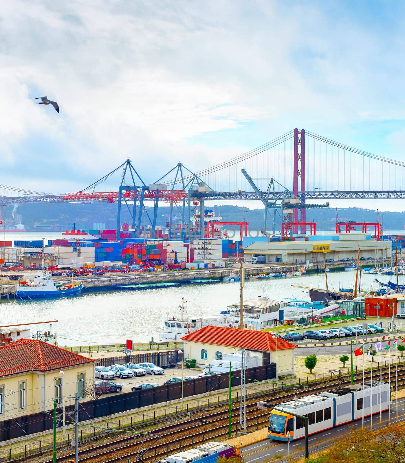 Seagulls over Lisbon commercial port, ships containers and freight cranes, skyline with 25th April Bridge and Tagus river, Portugal