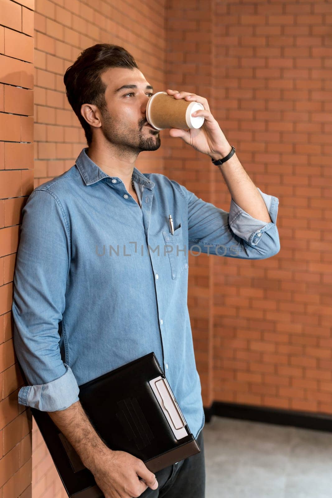 Portrait of middle east caucasian businessman drinking coffee from takeout disposable coffee cup and clipboard in meeting room after lunch break.