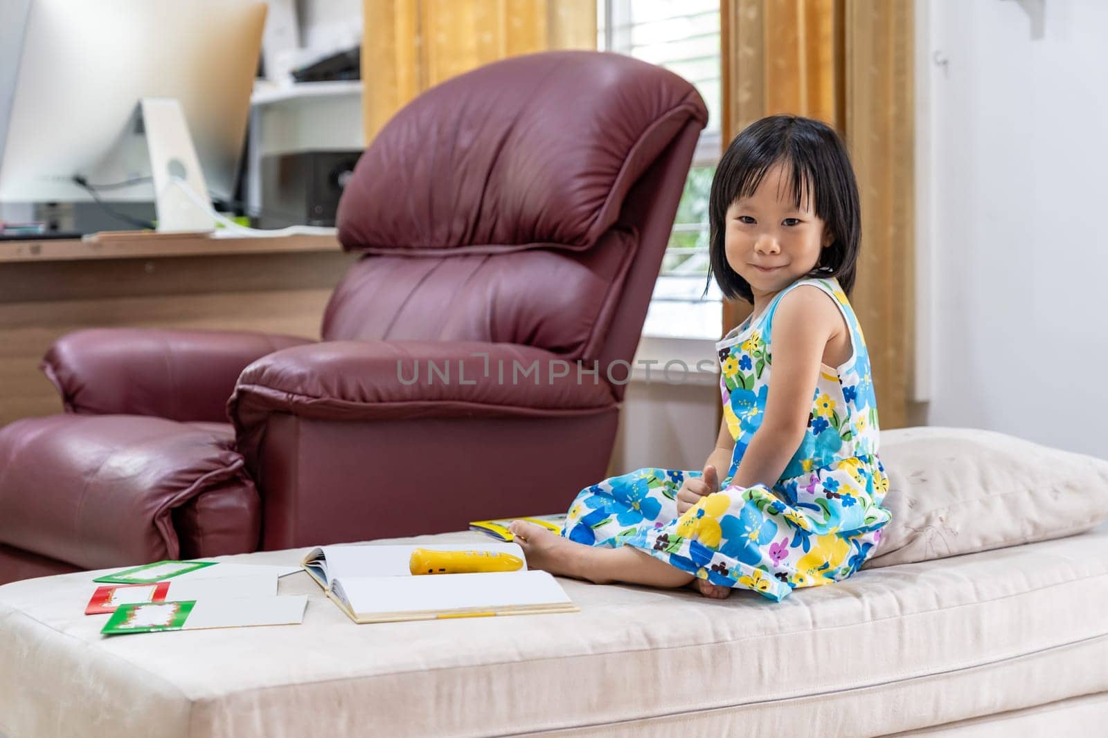 Portrait of Happy asian girl child reading interactive book in living room at home as home schooling while city lockdown because of covid-19 pandemic across the world. Home Schooling concept.