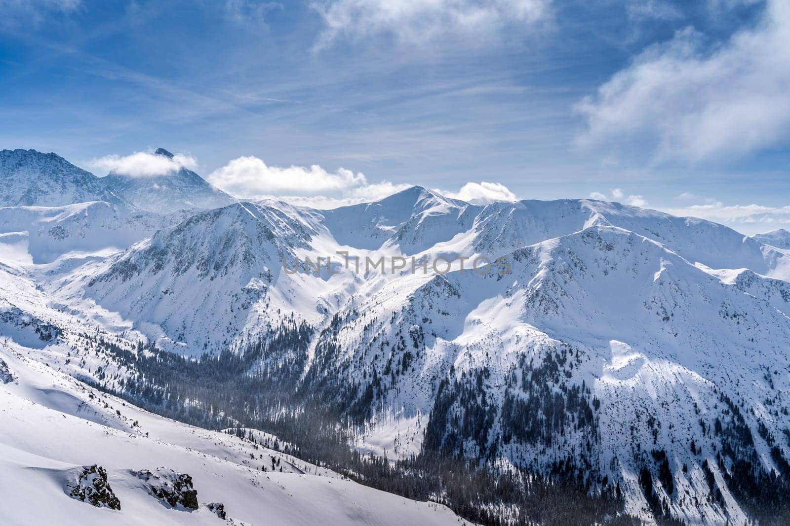View from Kasprowy Wierch at pine forest with winter coating in the valley. Snow capped mountain peaks of Tatra Mountains, Bukowina Tatrzanska, Poland