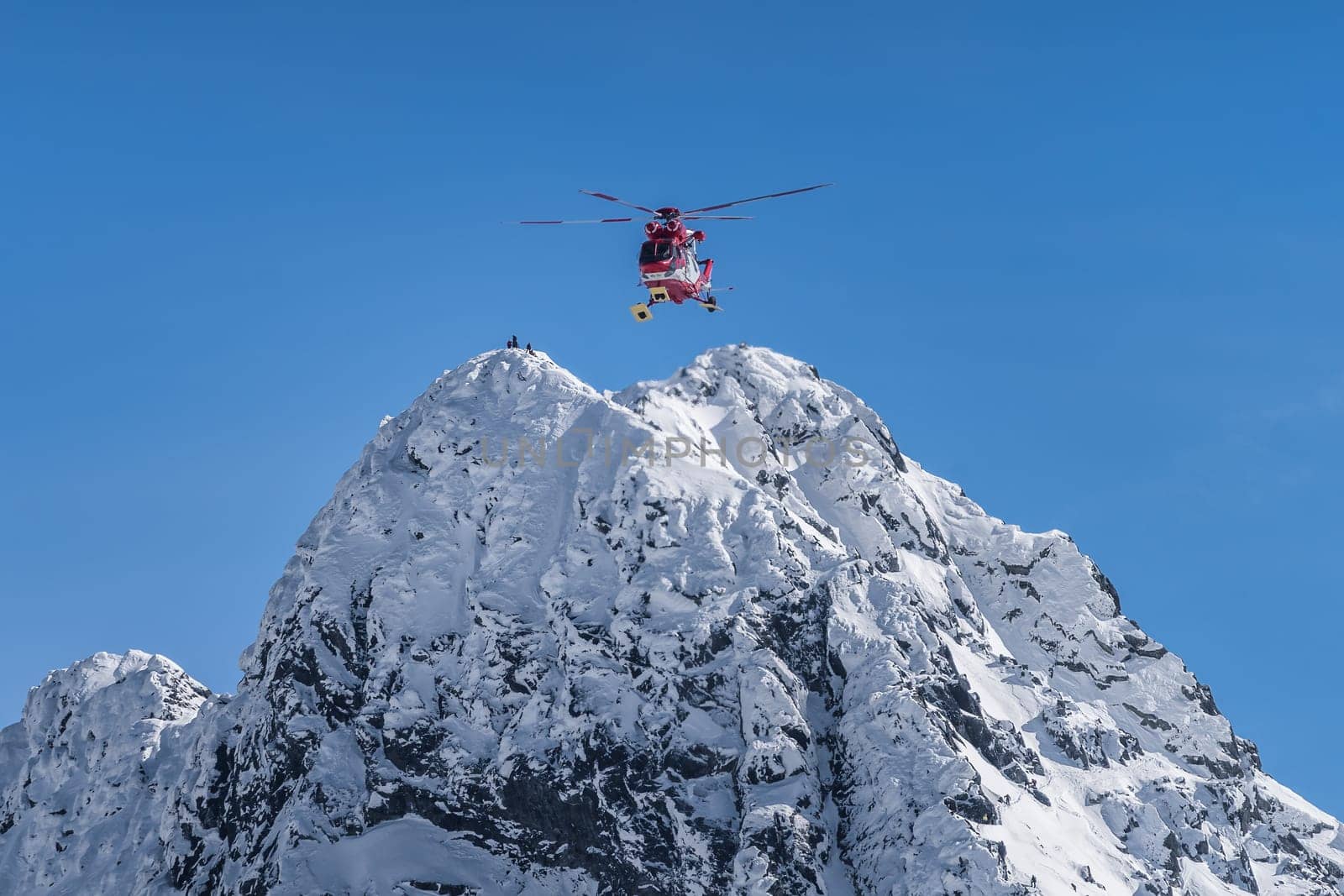 Rescue helicopter saved mountain climbers. People on the top of Swinica steep and rocky mountain peak at winter, Tatra Mountains, Poland