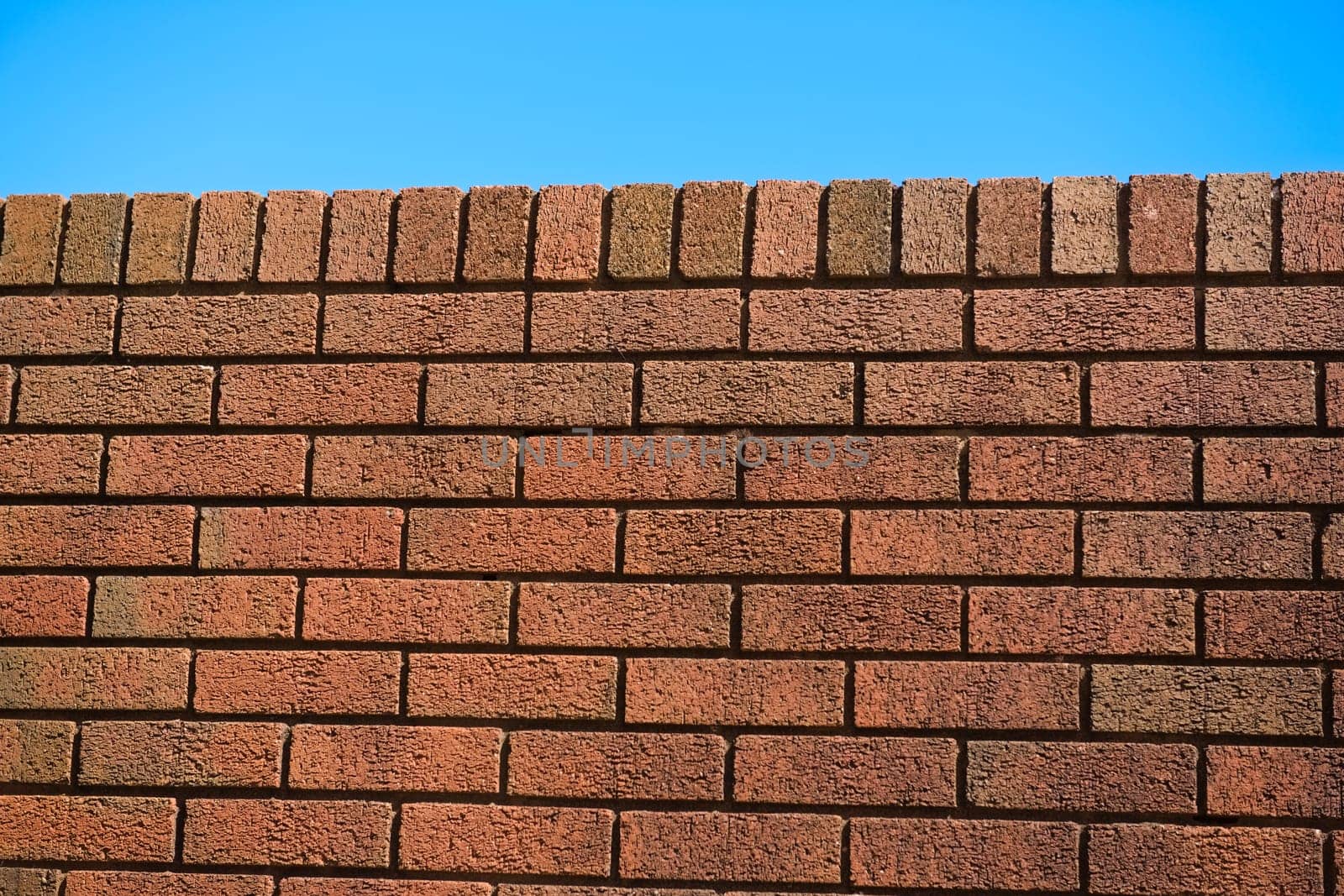 5 - Slanted view of red brick wall on a very bright and sunny day. Red color pops and stands out against the blue sky background. Colorful texture
