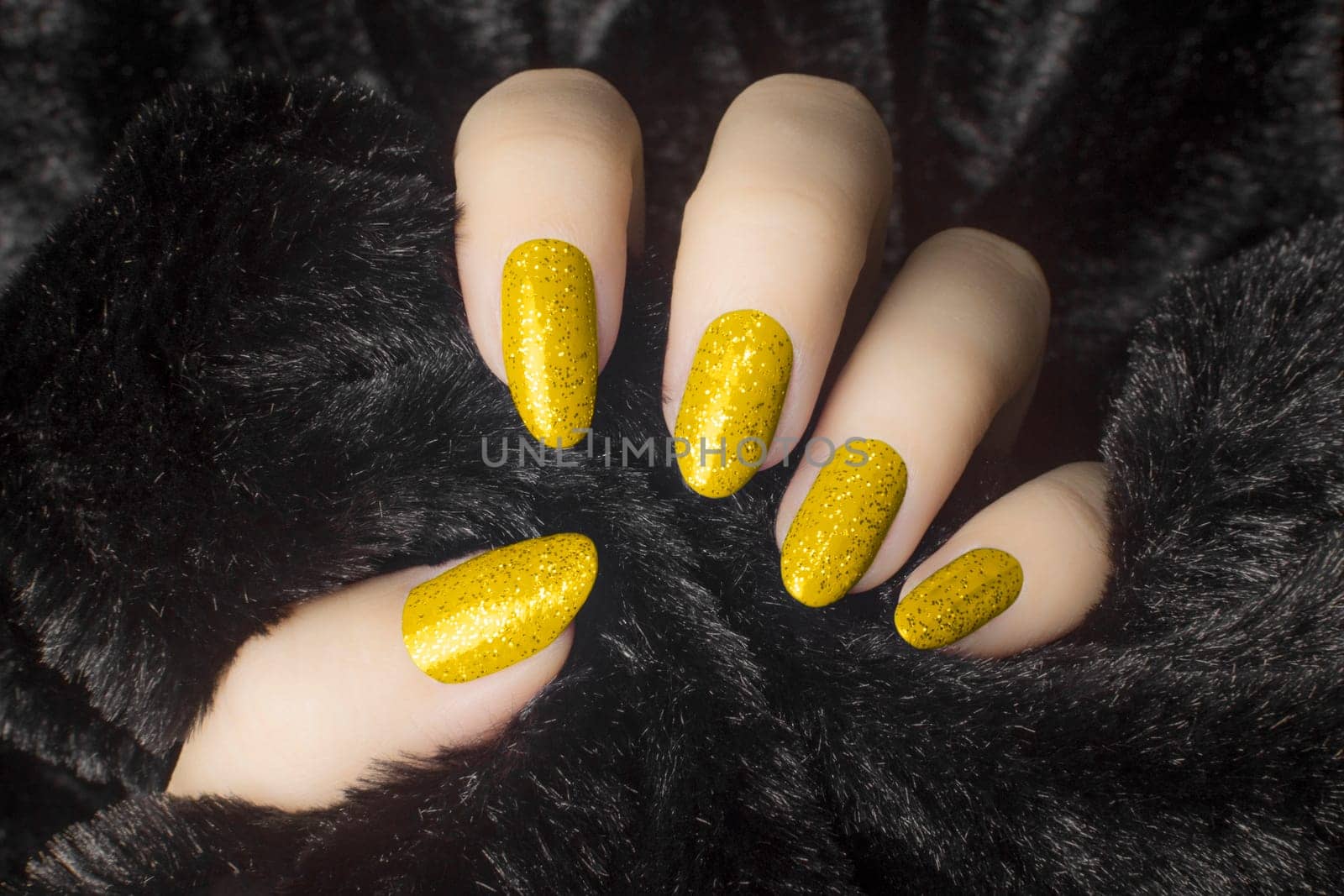 Female hand with glittered yellow nails is holding black fur, manicure and nail care concept.