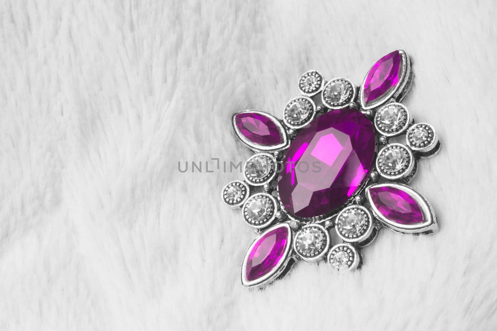 Beautiful luxurious brooch jewel or jewelry with pink gem on white fur background.