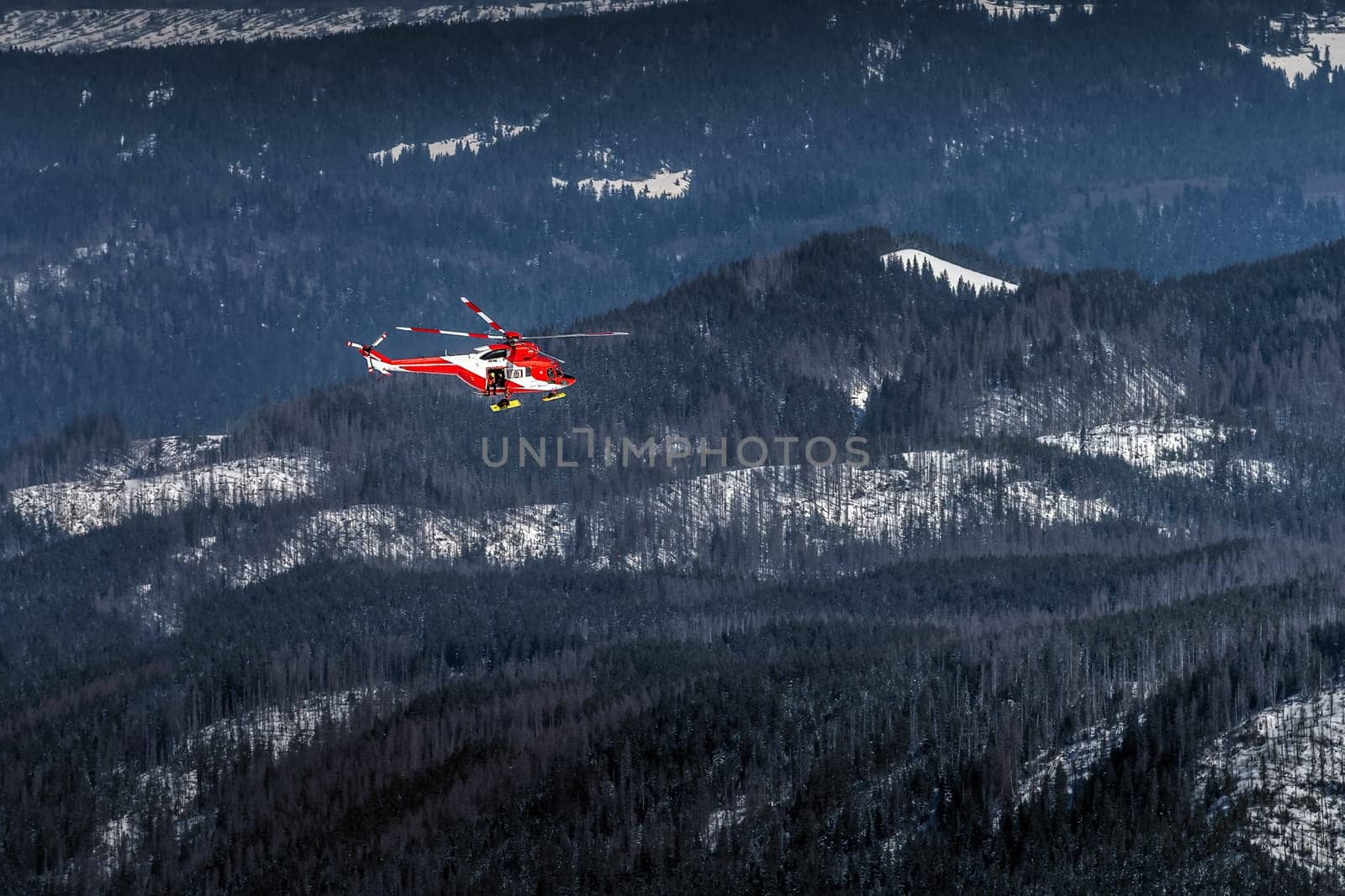 Red and White helicopter, rescue team or crew flying over dark forest in High Tatra Mountains, providing rescue service, Poland