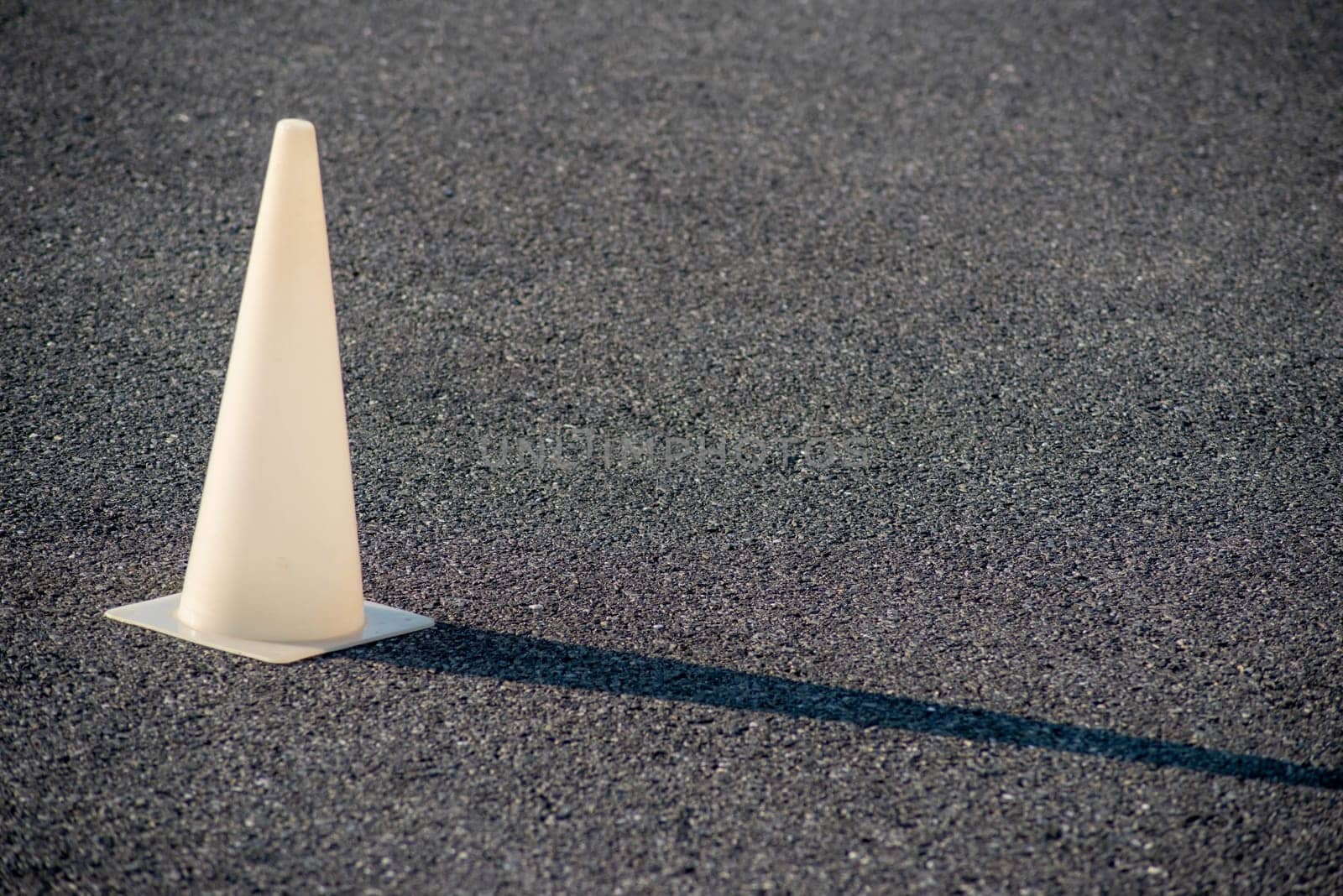 Full frame image with copy space shot in natural light. White plastic cone glows in golden hour sun and casts a long shadow on the black asphalt.