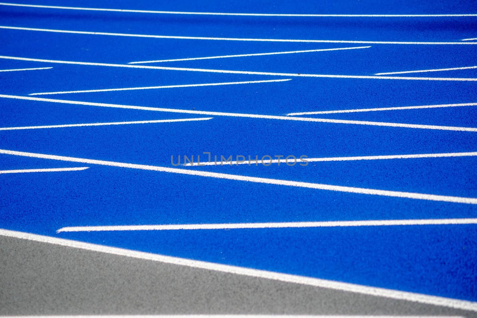 Full frame image in natural light of textured surface of a clean, new outdoor blue running track with white lines and copy space.