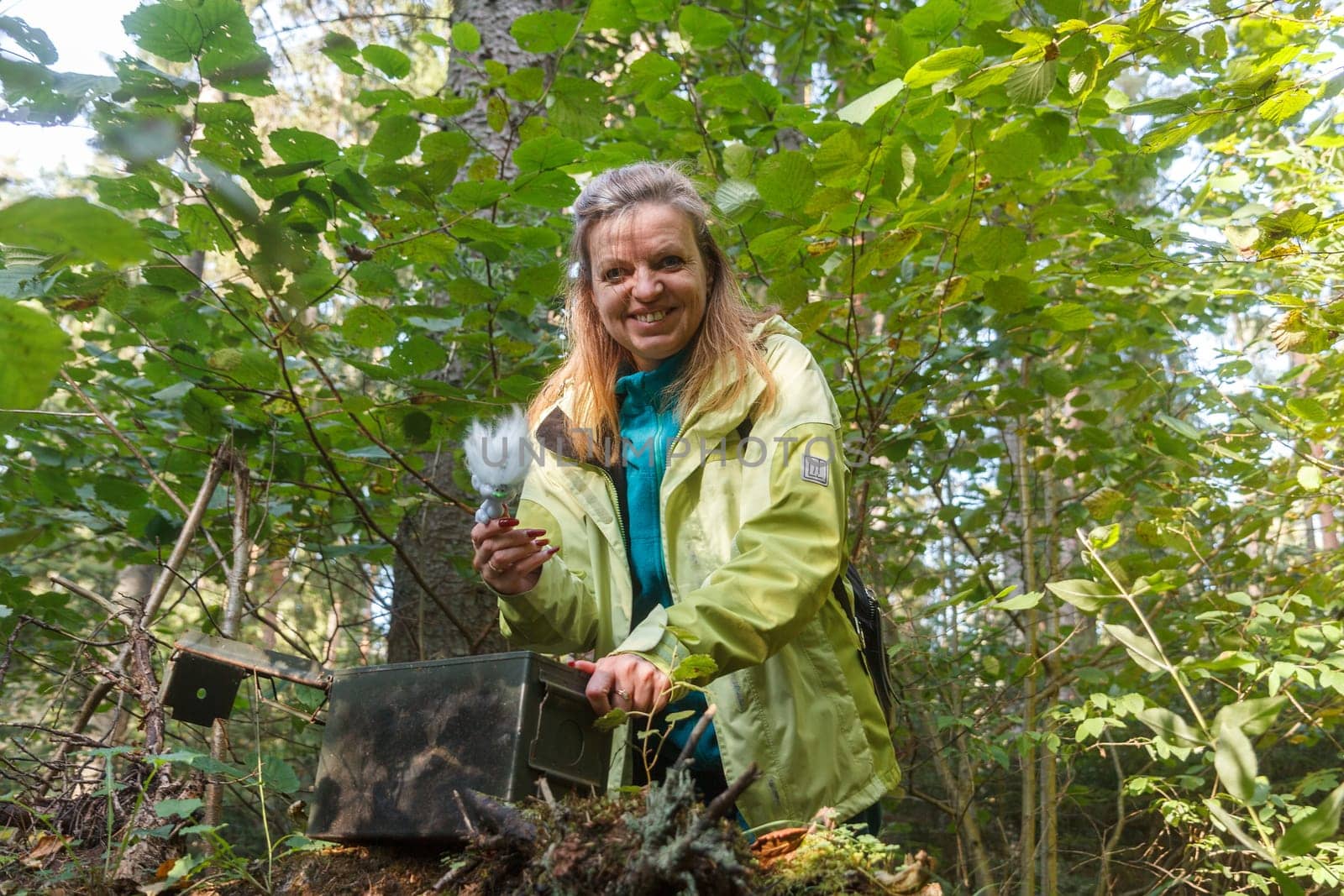 A woman geocaching. Women in woods find geocache container. Big ammo box with log book and some toys.