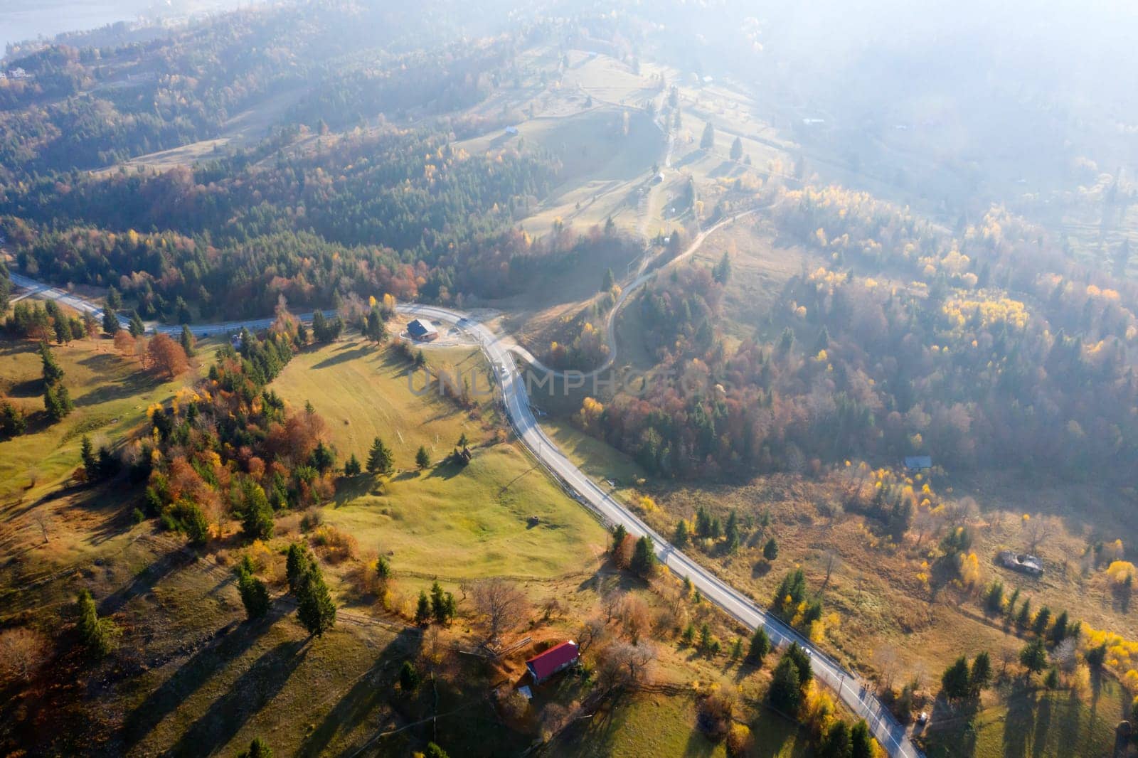 Aerial view of road in beautiful autumn forest at sunset.