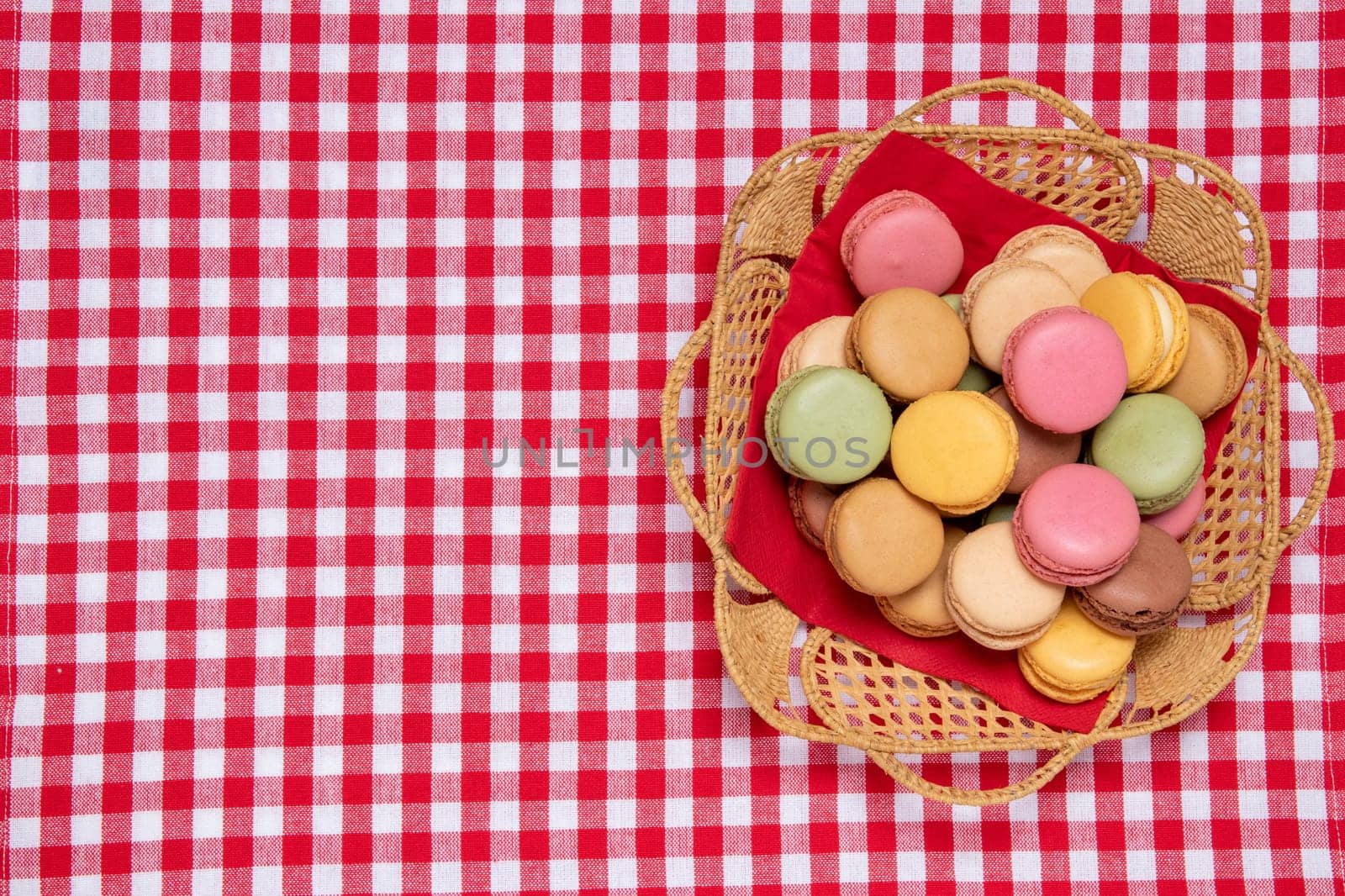 Pastries, desserts and sweets. Top view of multicolord original french macaroon cookies are arranged in a basket on a red checkered napkin. Party, birthday and invitation concept. Copy space.