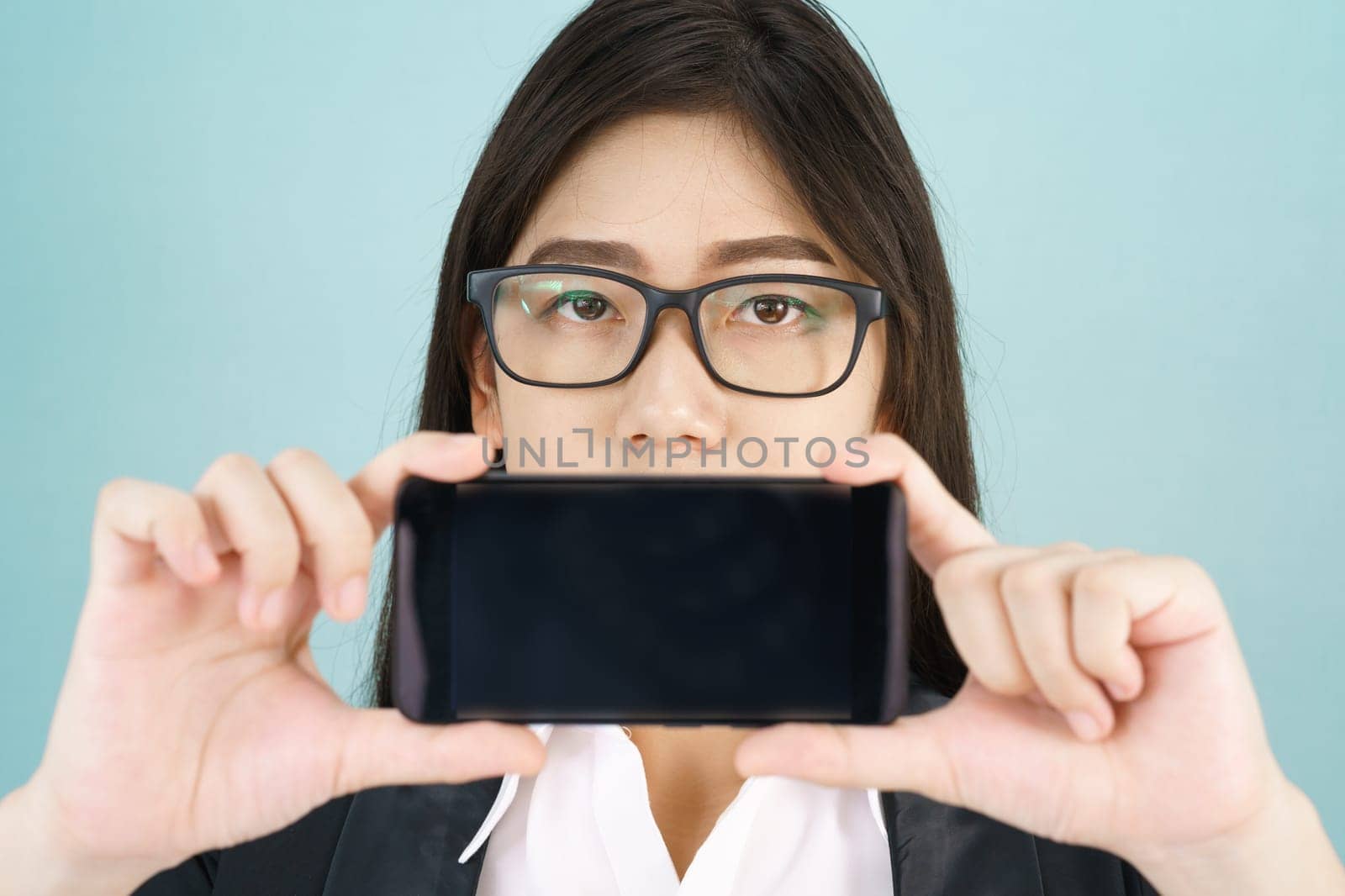 Young women in suit holding her smartphone standing against blue background