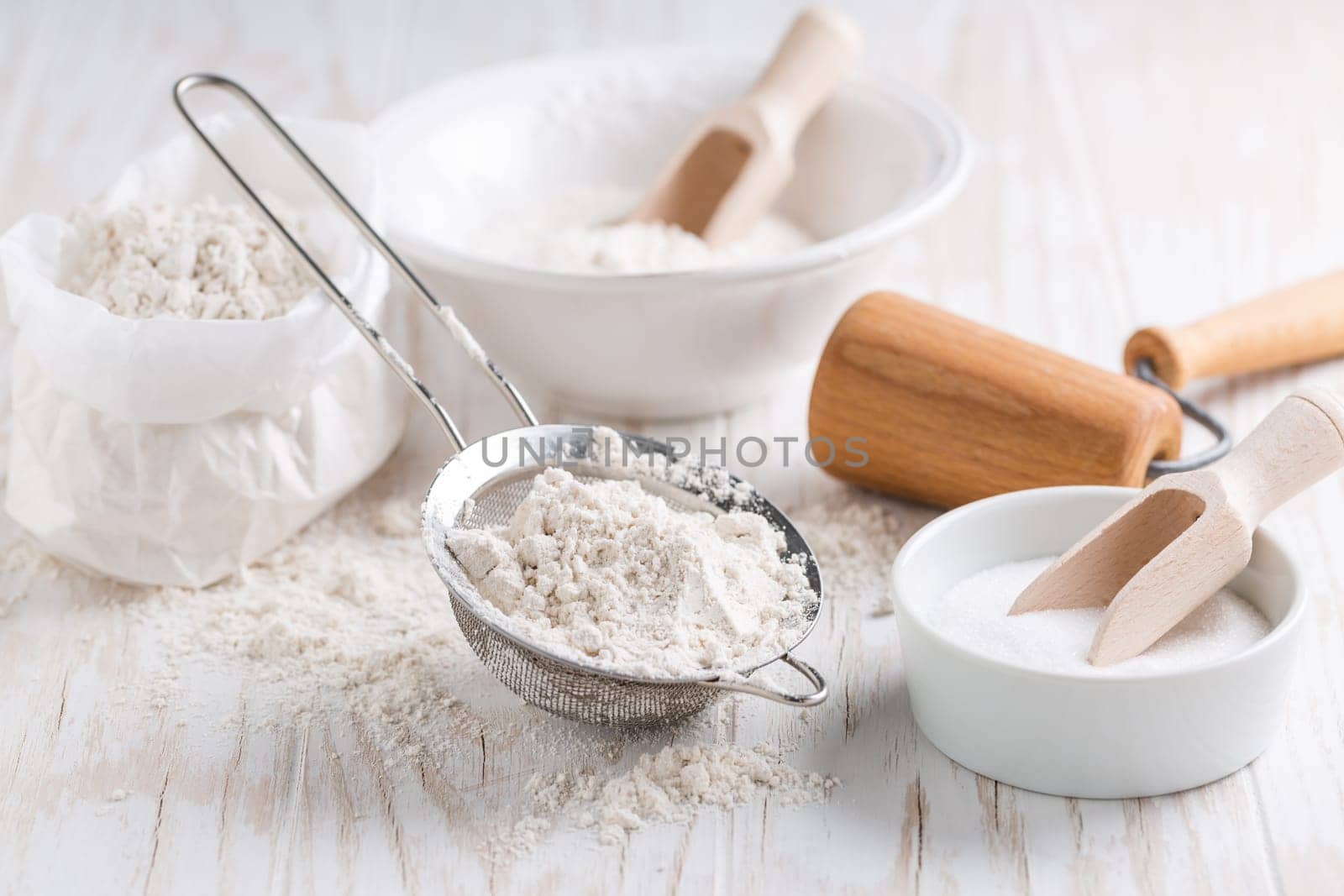 Spelt flour, sugar with baking ingredients and kitchen utensils on white wooden table.