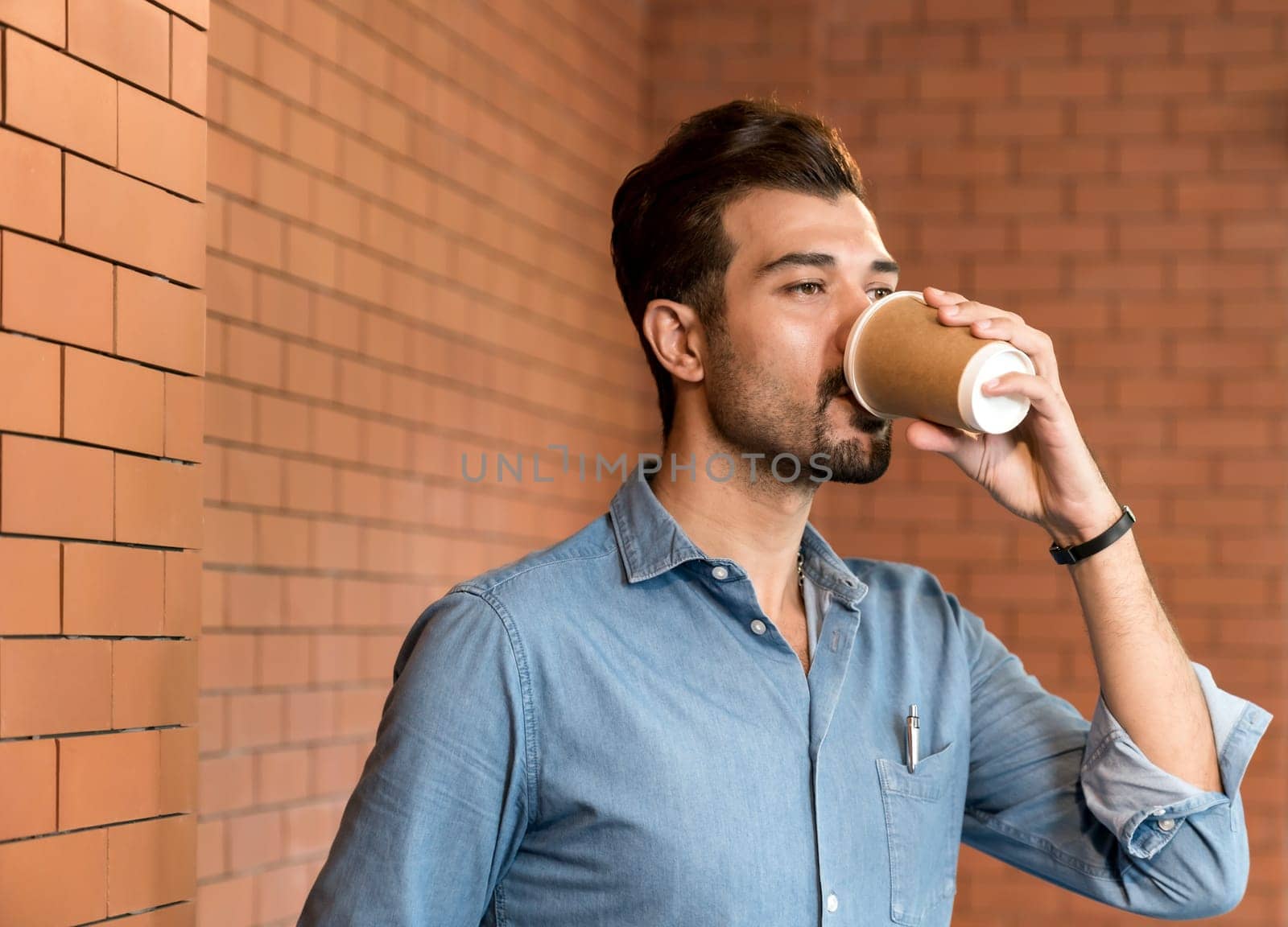 Portrait of middle east caucasian businessman drinking coffee from takeout disposable coffee cup and clipboard in meeting room after lunch break.