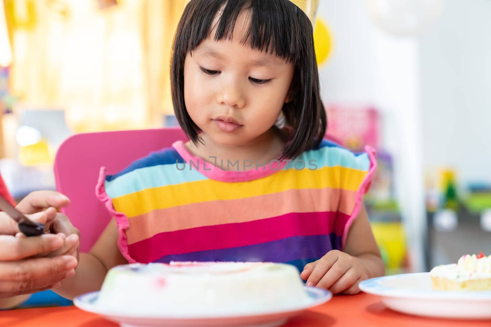 Asian girl kid cutting her birthday cake celebrate with mom alone because city lockdown while COVID-19 Pandemic. Celebration and quarantine concept.