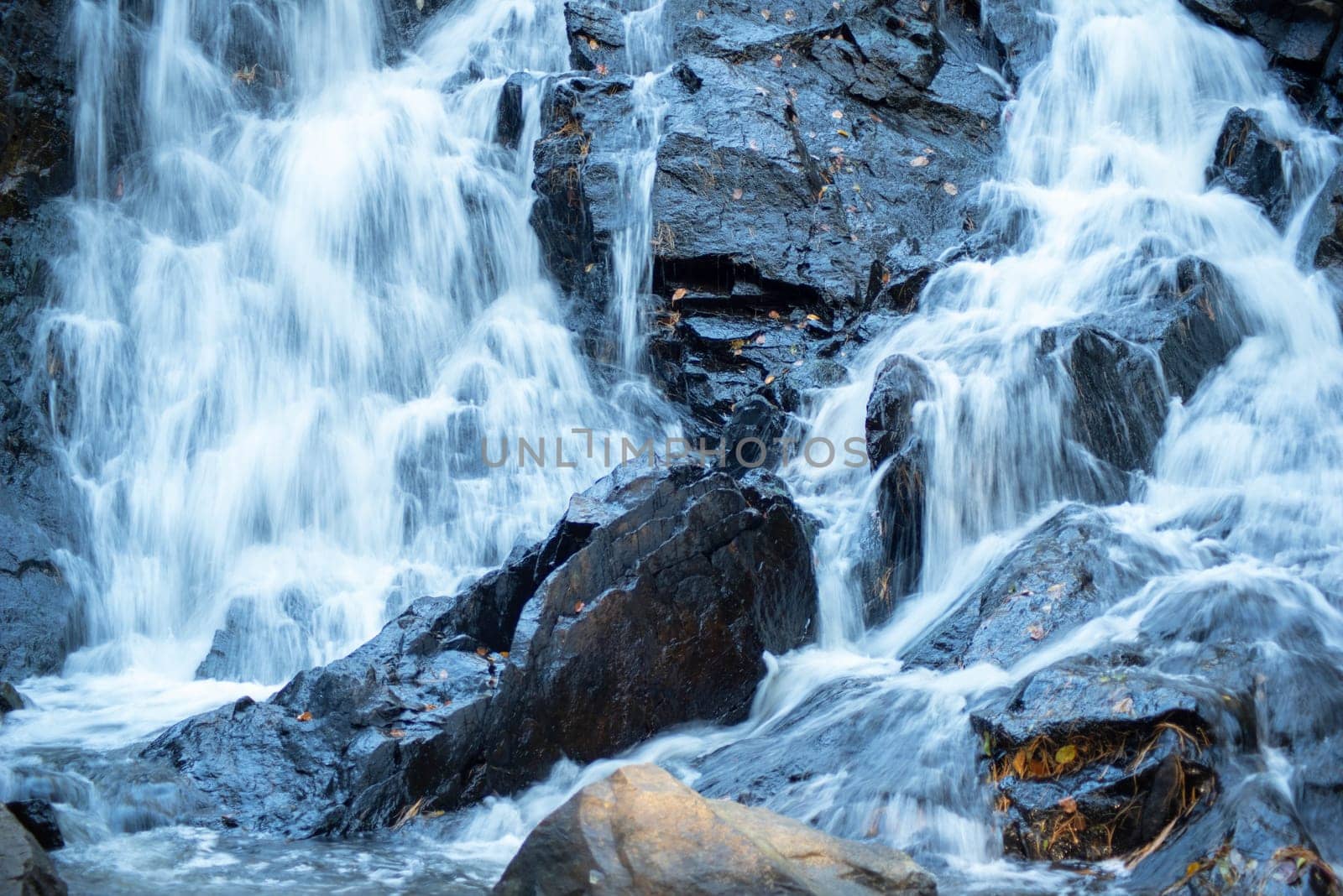 Long exposure water cascades around a rough textured black rock. Full frame in natureal light with copy space.