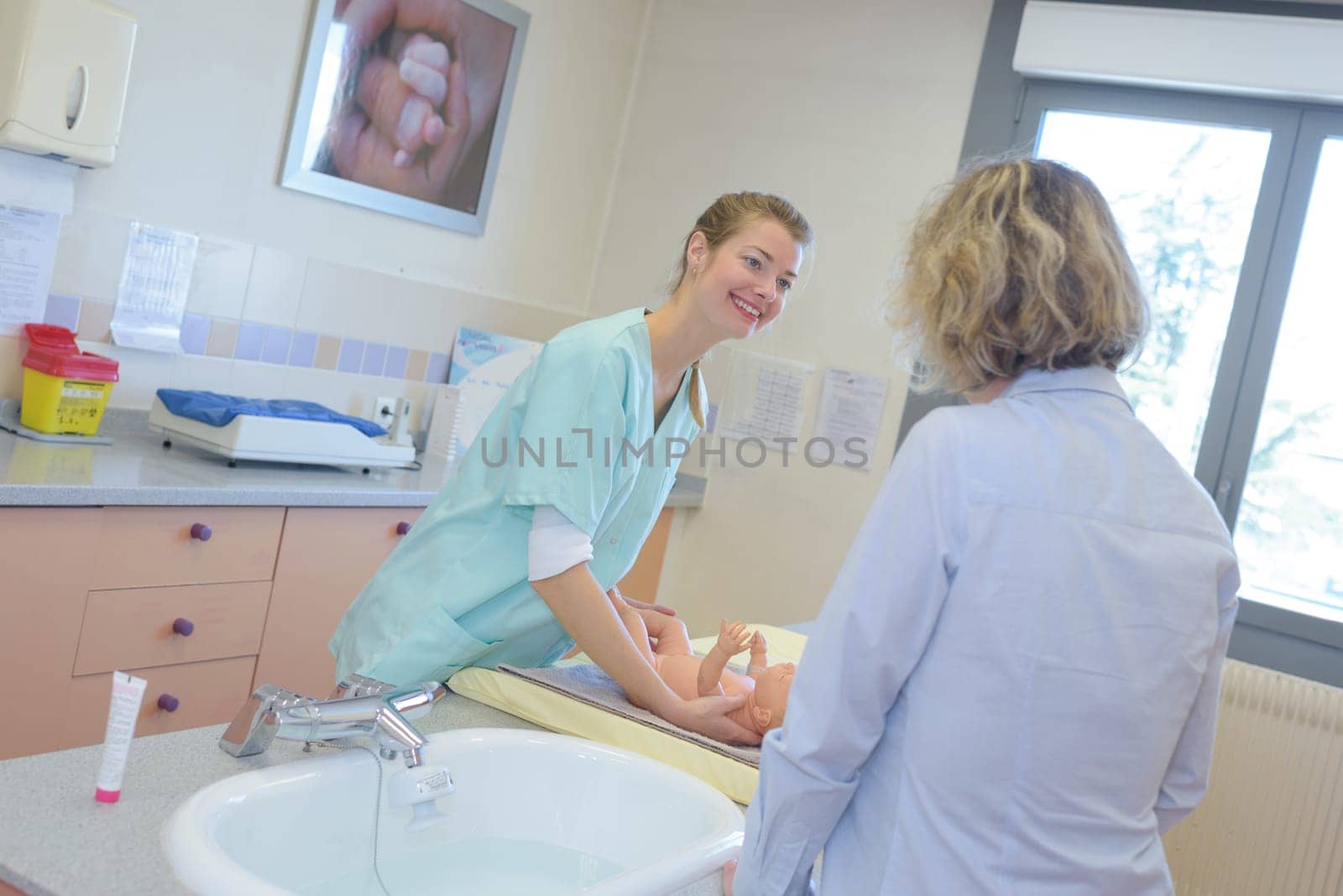 female nurse caring baby near his mother at the hospital