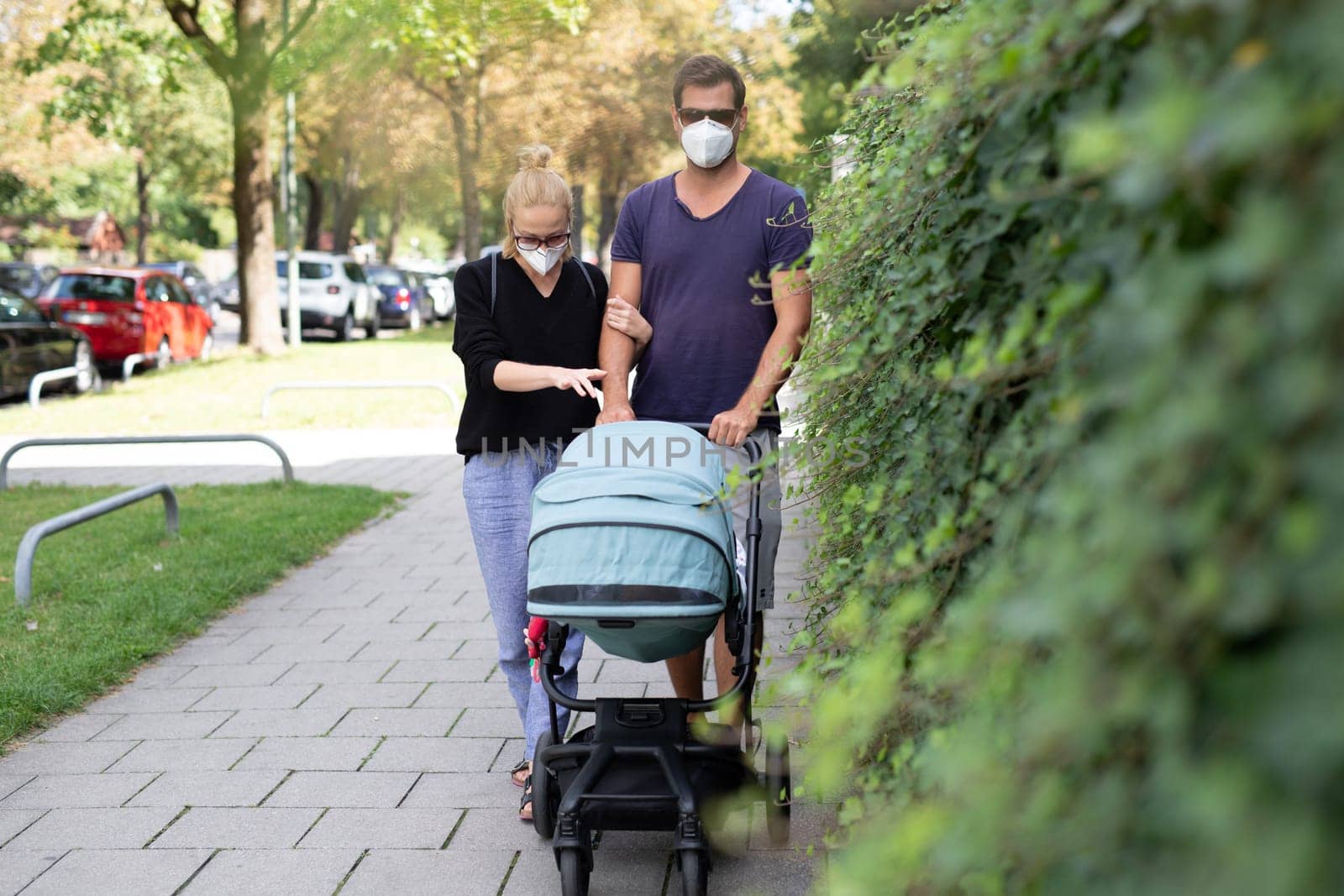 Worried young parent walking on empty street with stroller wearing medical masks to protect them from corona virus. Social distancing life during corona virus pandemic.
