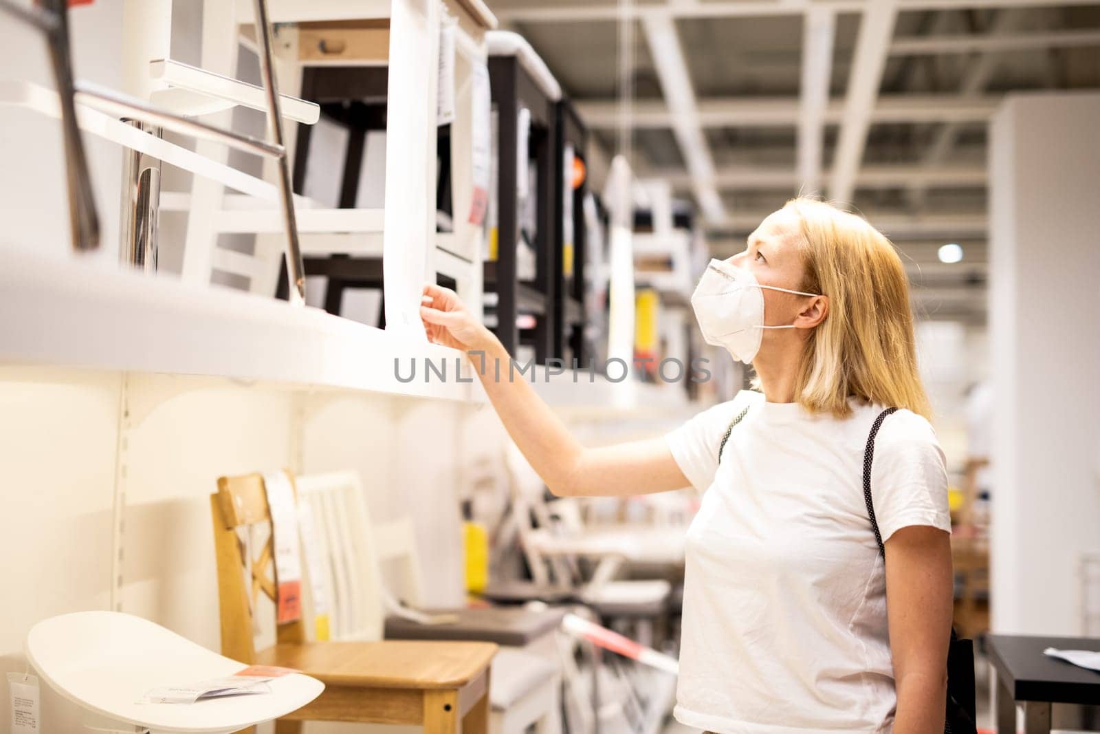 New normal during covid epidemic. Caucasian woman shopping at retail furniture and home accessories store wearing protective medical face mask to prevent spreading of corona virus.