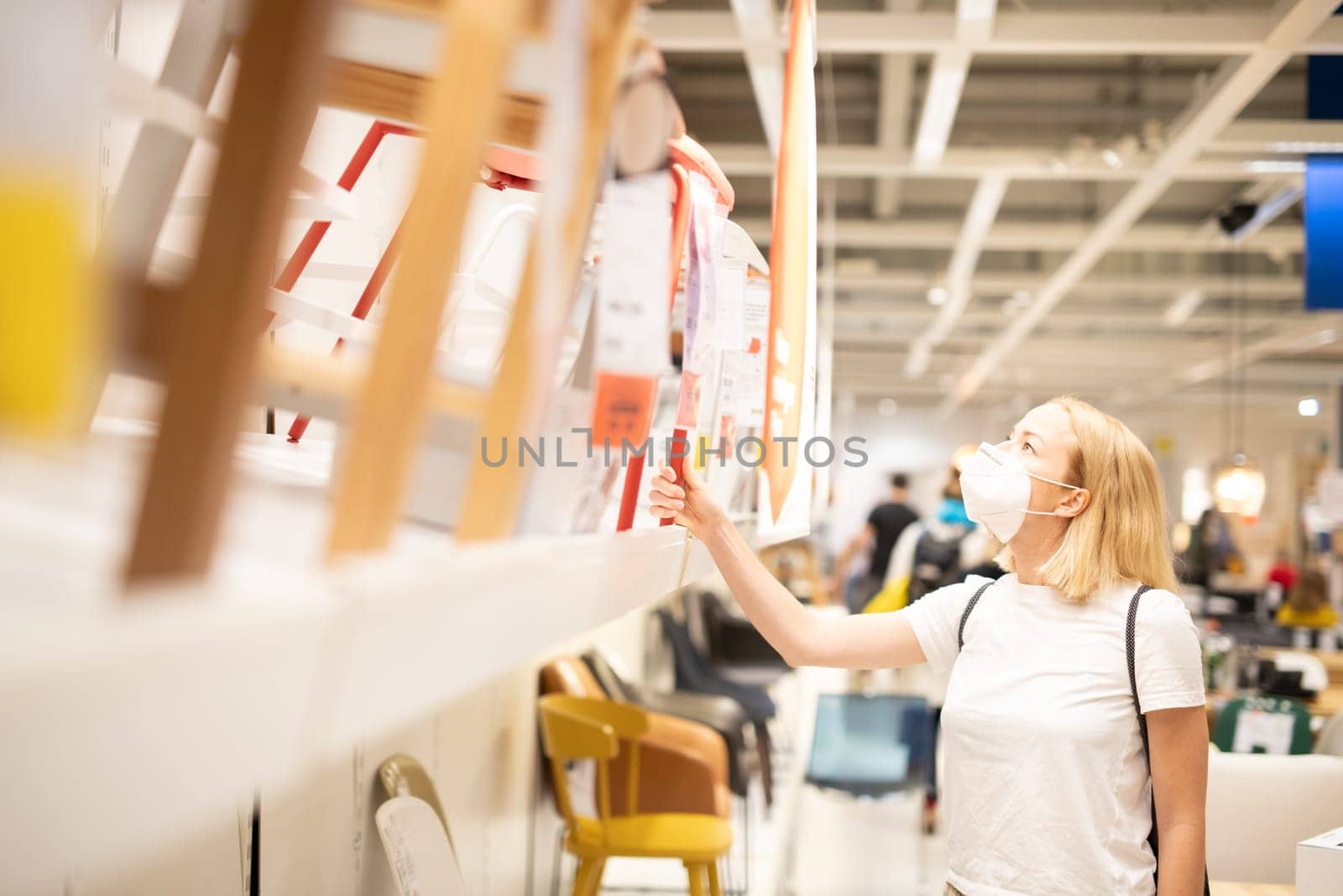 New normal during covid epidemic. Caucasian woman shopping at retail furniture and home accessories store wearing protective medical face mask to prevent spreading of corona virus.