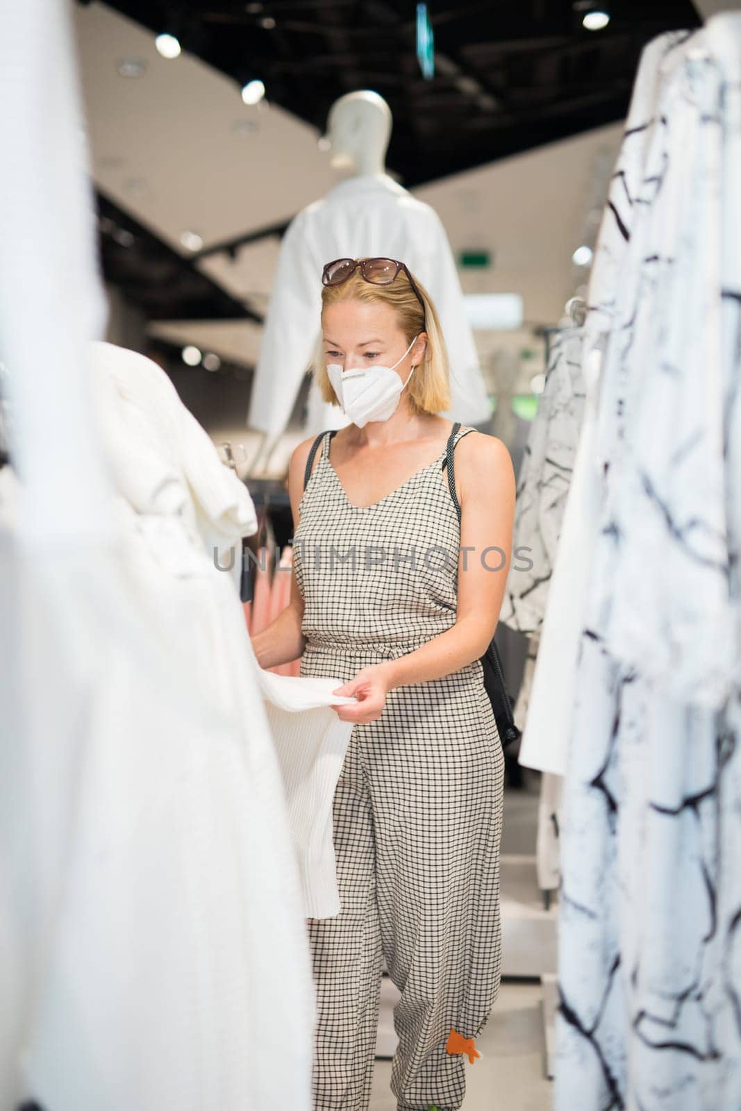 Fashionable woman wearing protective face mask shopping clothes in reopen retail shopping store. New normal lifestyle during corona virus pandemic.