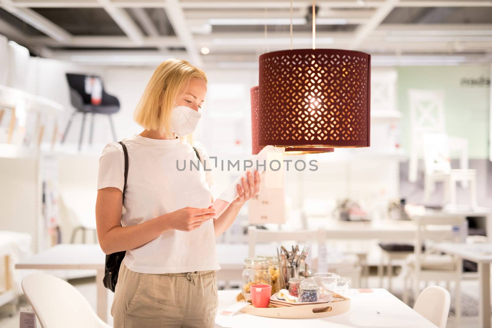 New normal during covid epidemic. Caucasian woman shopping at retail furniture and home accessories store wearing protective medical face mask to prevent spreading of corona virus.