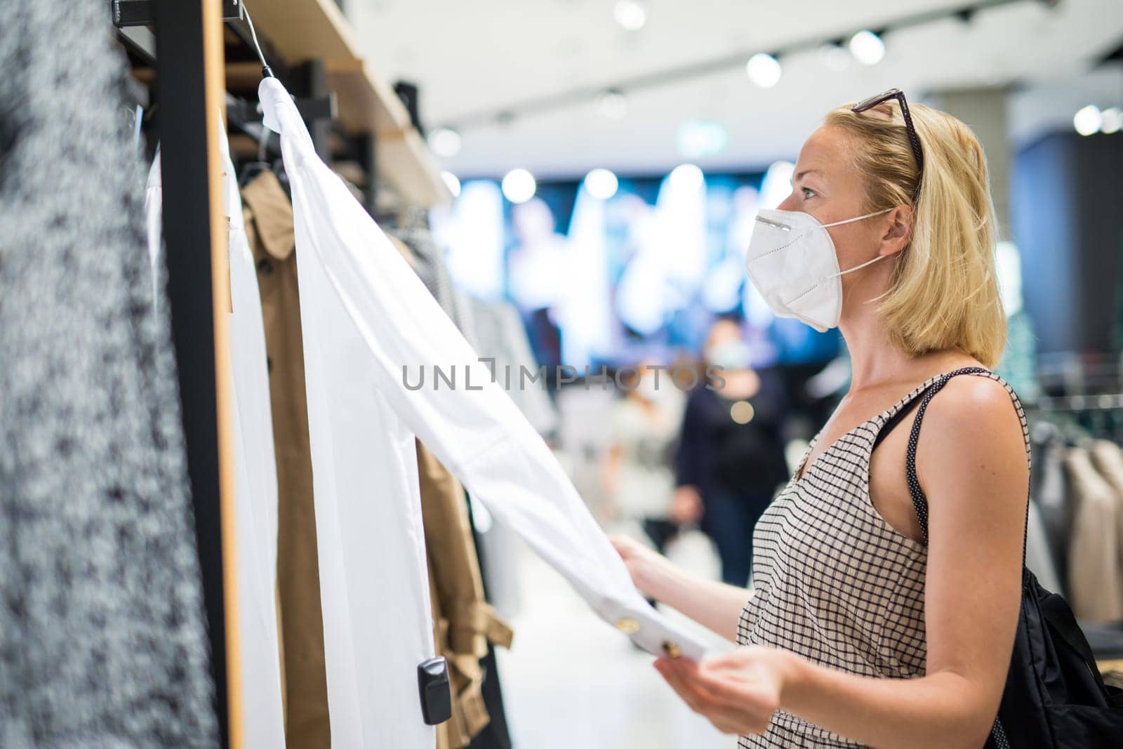Fashionable woman wearing protective face mask shopping clothes in reopen retail shopping store. New normal lifestyle during corona virus pandemic.