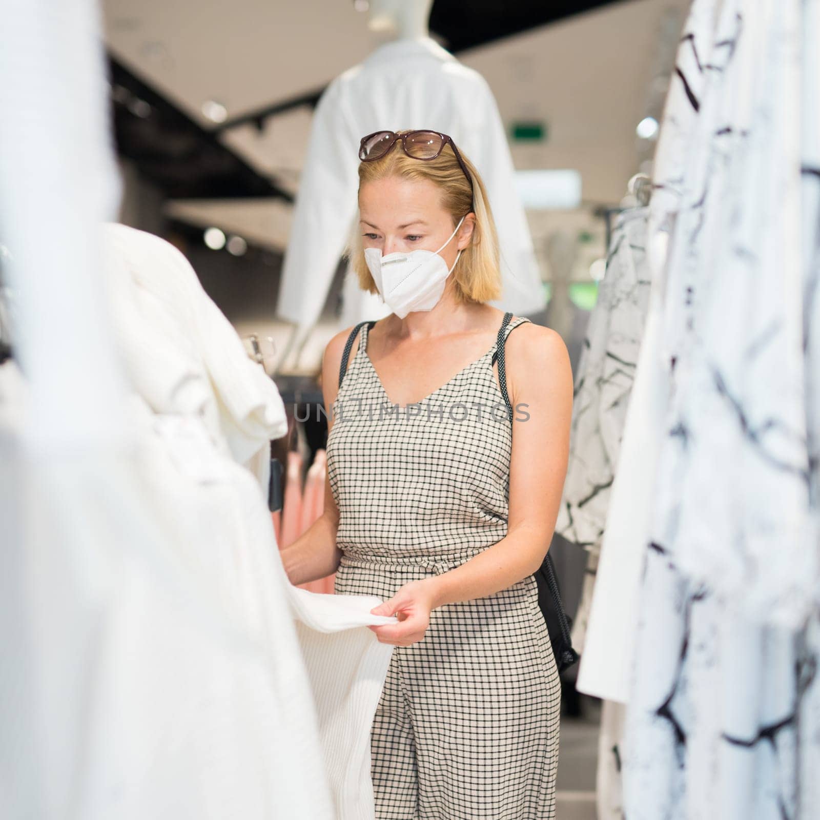 Fashionable woman wearing protective face mask shopping clothes in reopen retail shopping store. New normal lifestyle during corona virus pandemic.