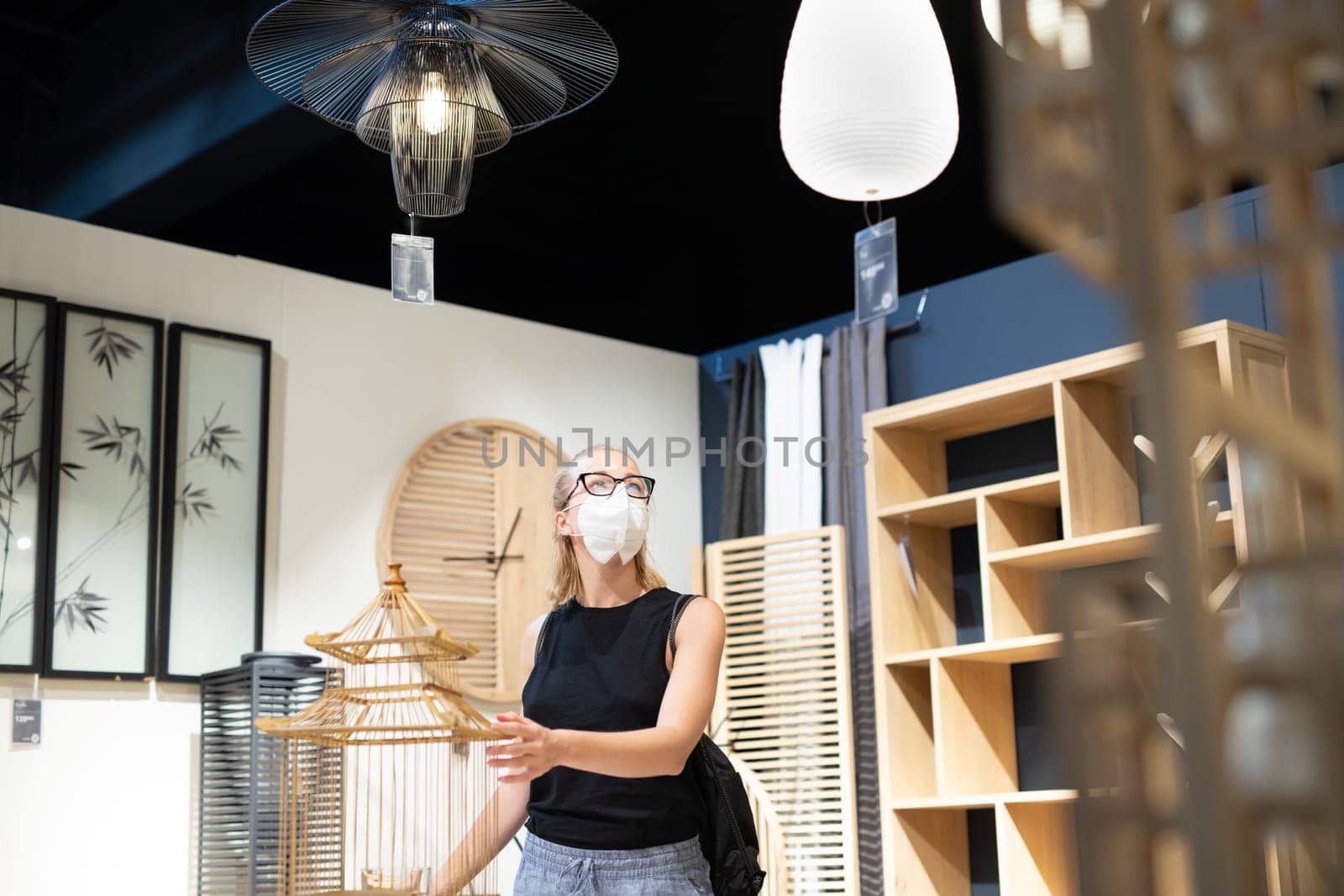 New normal during covid epidemic. Caucasian woman shopping at retail furniture and home accessories store wearing protective medical face mask to prevent spreading of corona virus.