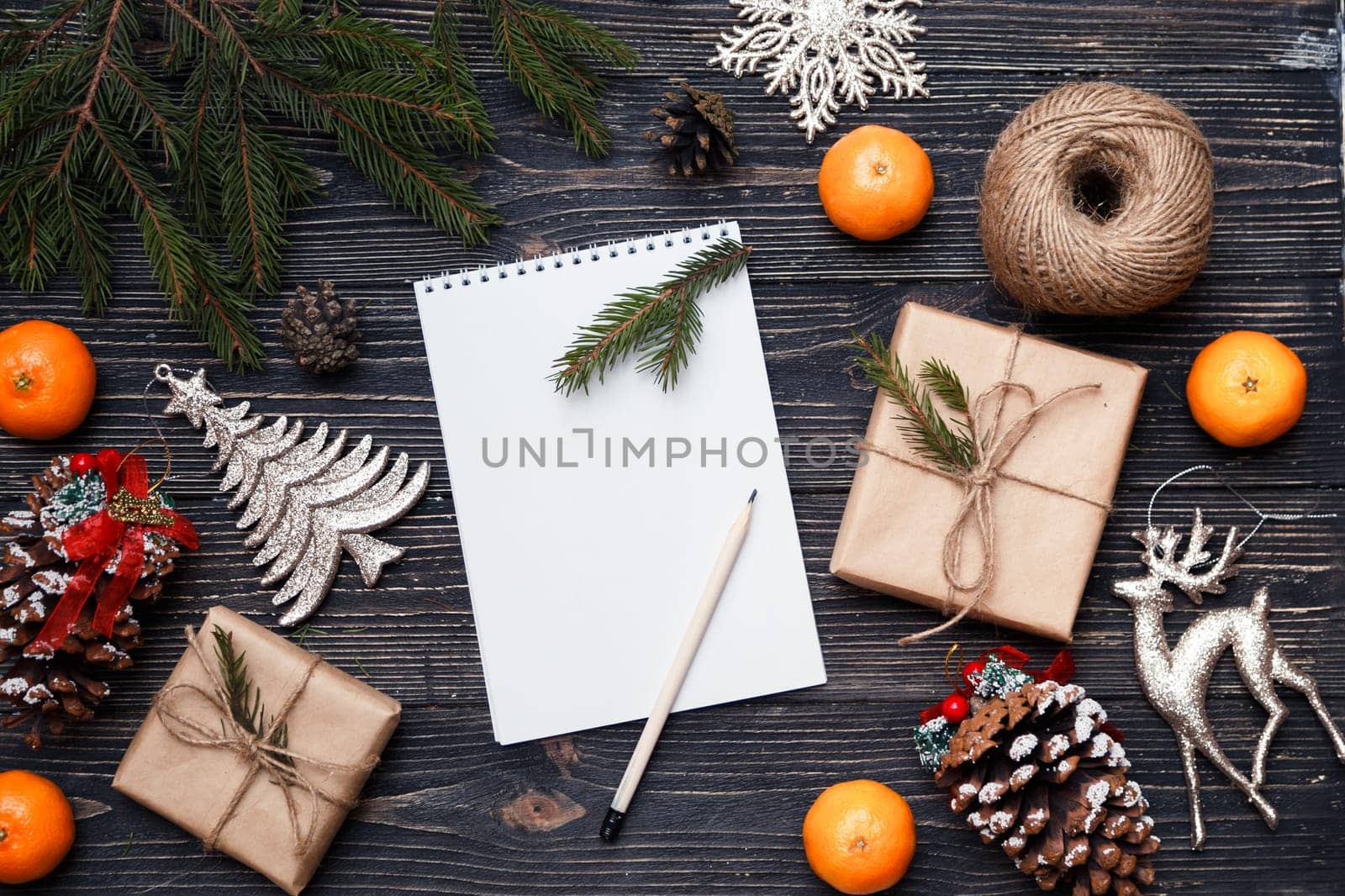 Blank note sheet with gifts boxes and decorations on black wooden background. Holiday time concept. top view.
