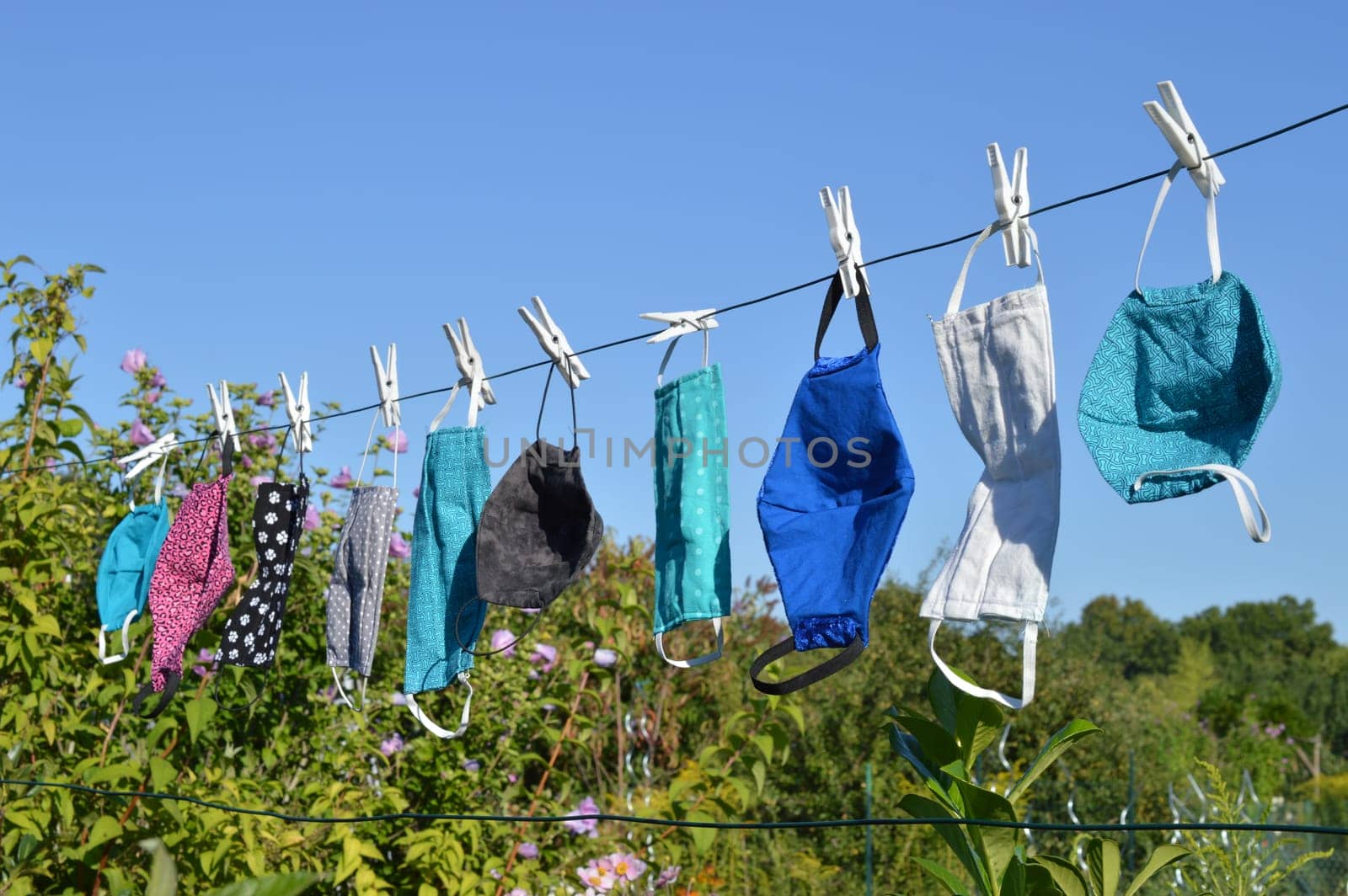 a lot of different colorful self made corona face masks out of fabric hanging on a clothesline for drying