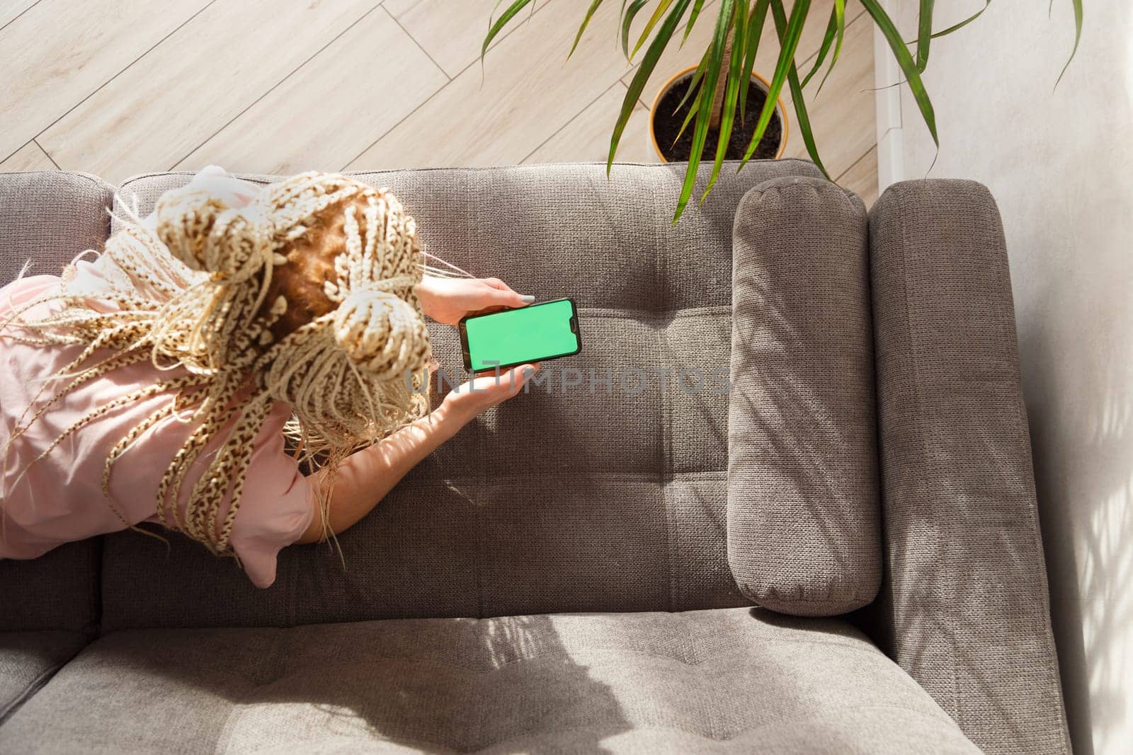 Woman with blond canecalons lying on a sofa use a smartphone with green screen for your image. Top view.