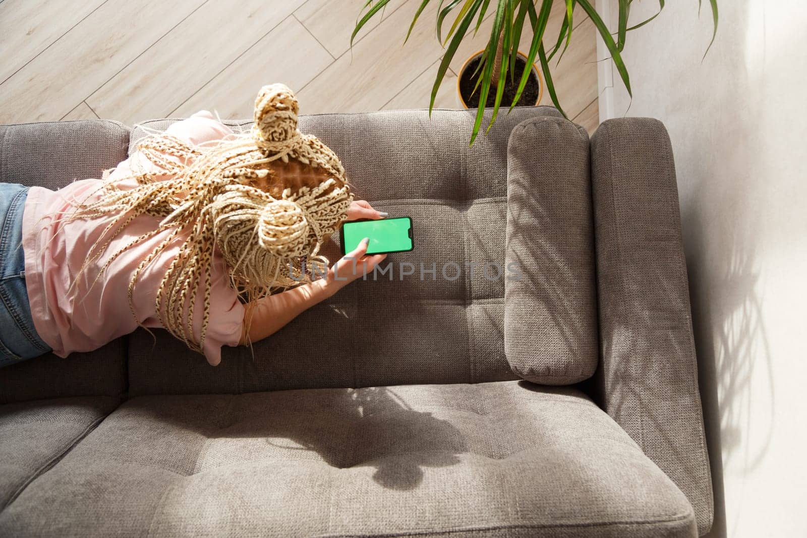 Woman with blond canecalons lying on a sofa use a smartphone with green screen for your image. Top view