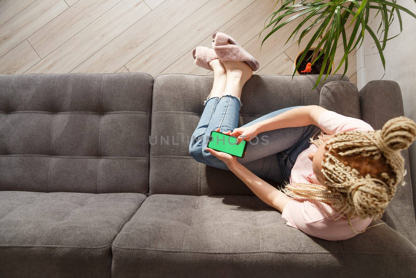 Woman with blond canecalons sitting on sofa and using smartphone with green screen for your image.