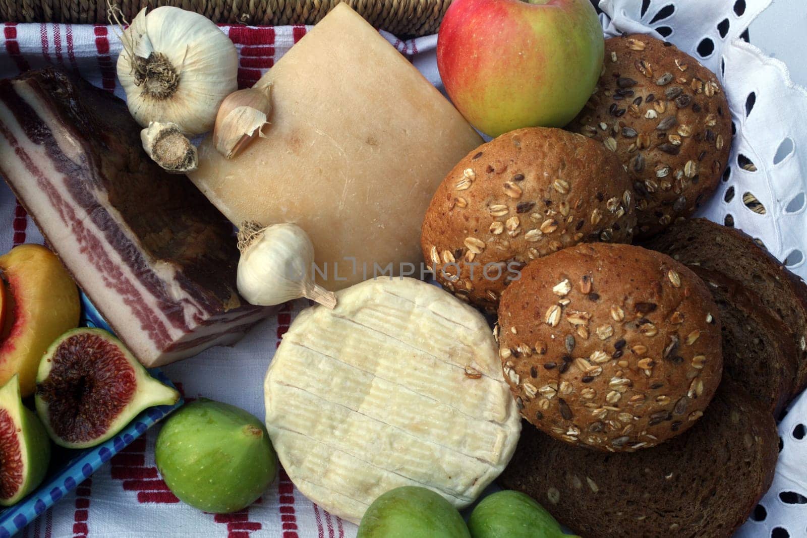 Rustic still life of bread, cheese, bacon and figs in a wicker basket