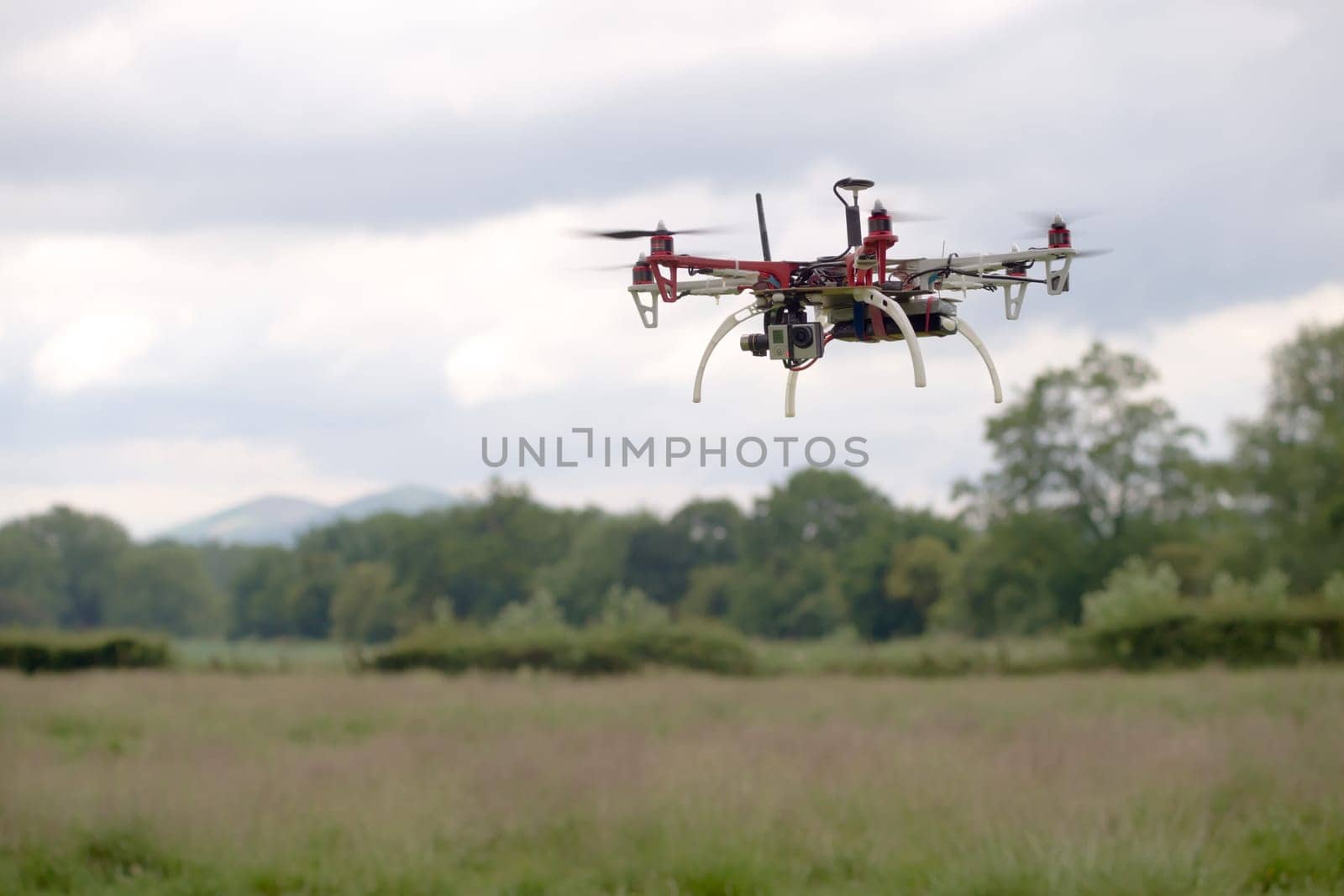 Large hex copter camera drone hovers in front of a rural back ground of the malvern hills. Autonomous FPV modern flight, gimbal stabilized camera