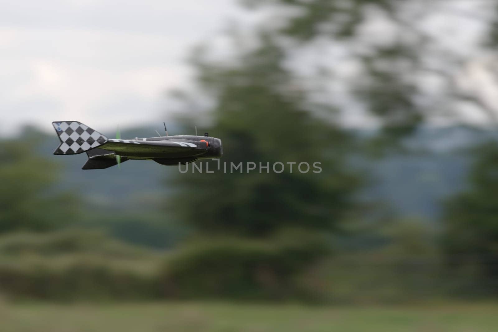 Pan shot technique creates a blurred background as this remote control delta FPV drone flies pas at high speed. Rural background and racing pattern.