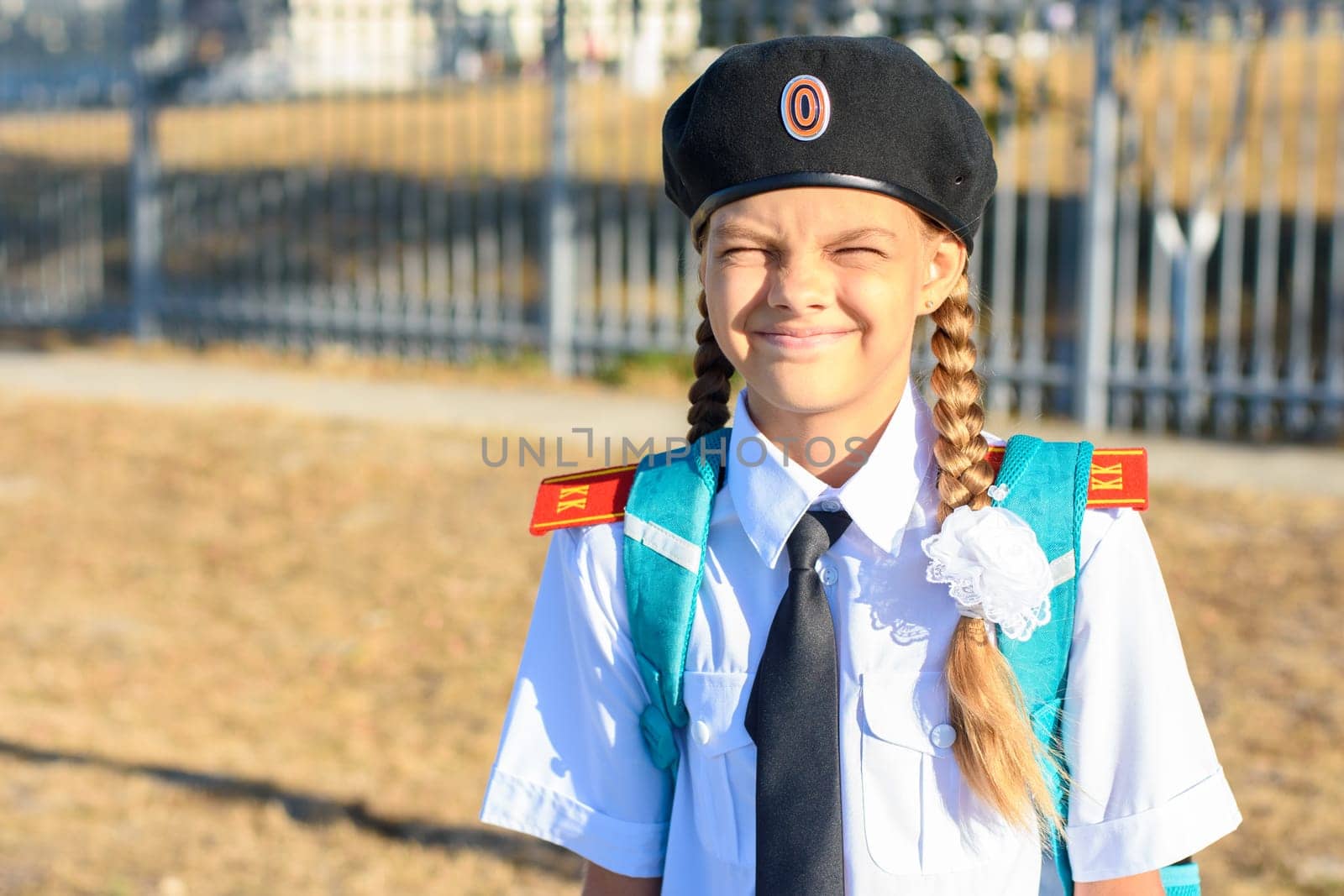 A girl in the uniform of a Cossack cadet smiles cheerfully and closed her eyes from the sun